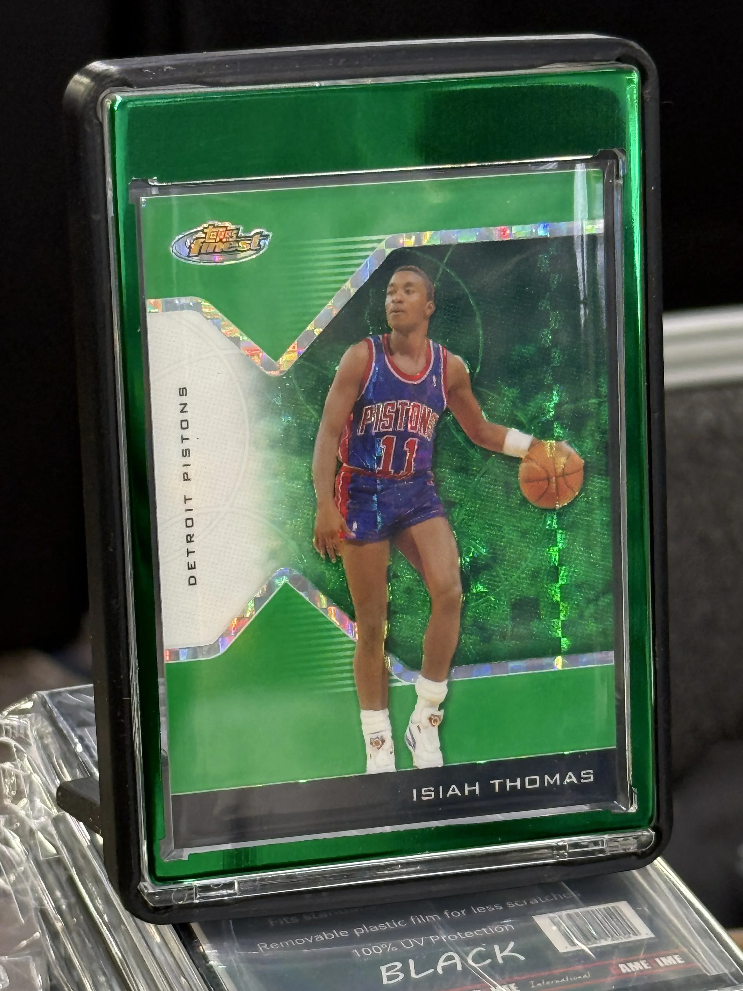A basketball trading card of Isiah Thomas in a green protective case.