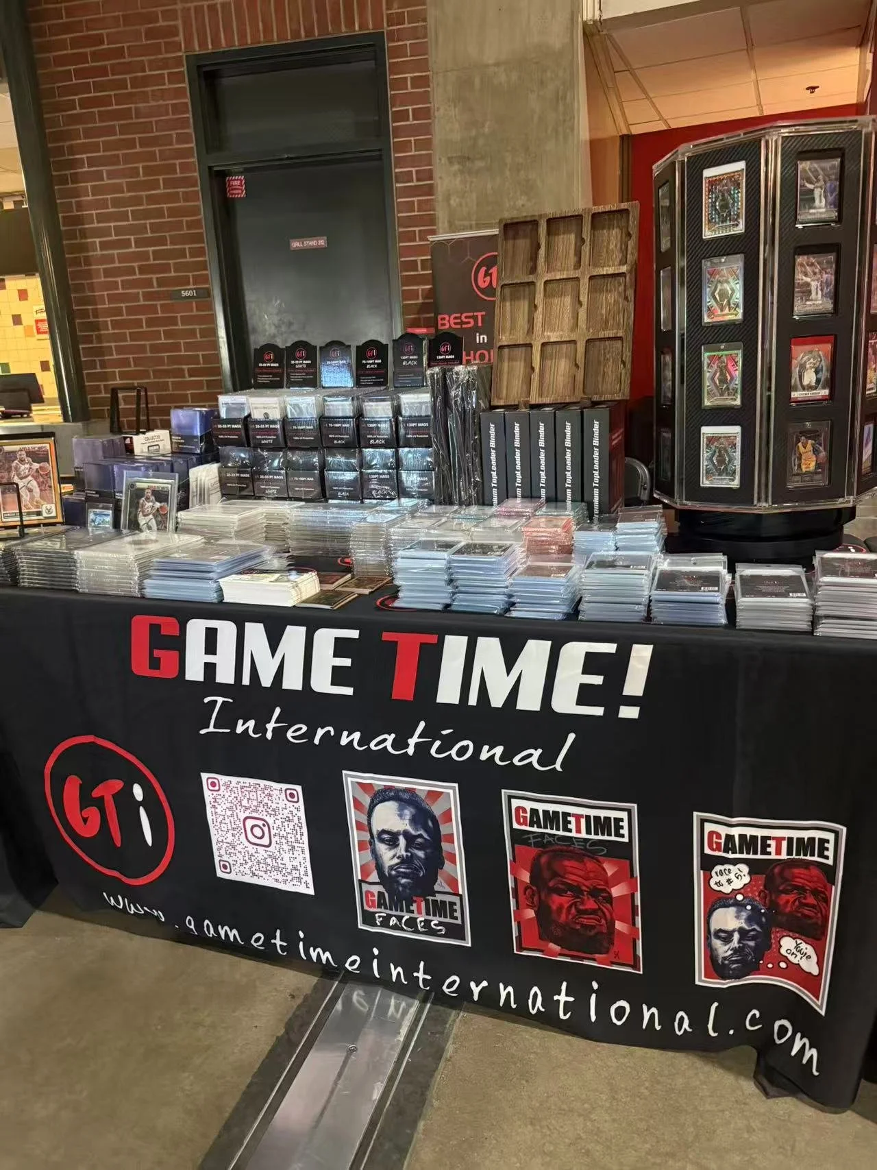 A display table at a gaming convention with various trading cards and card protectors, featuring a banner that reads 'GAME TIME! International' and the website gametimeinternational.com.