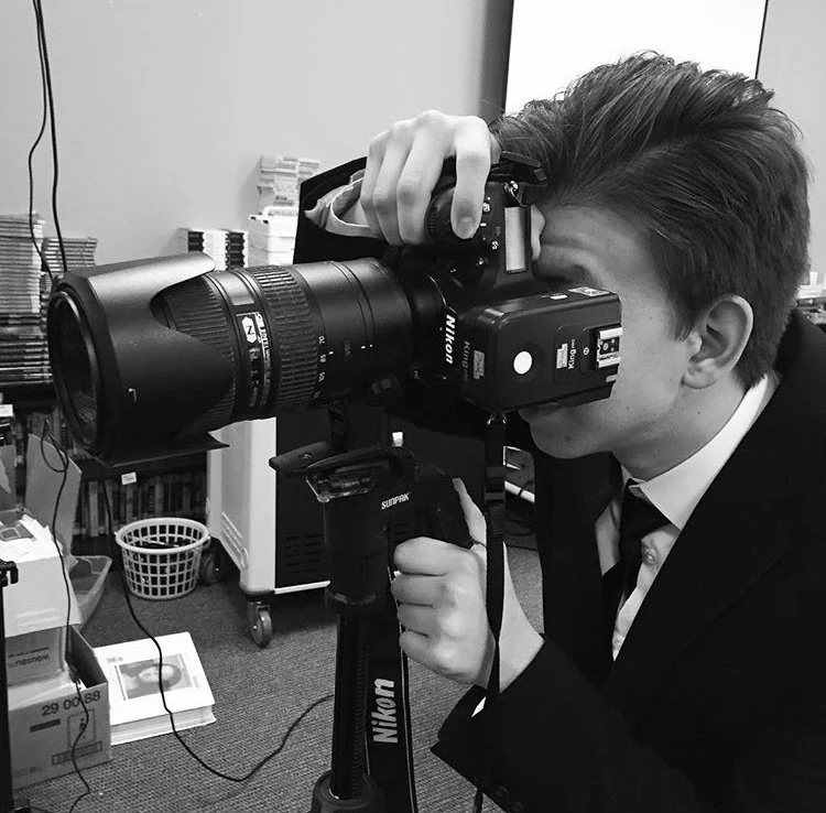 A wedding photographer in Dallas in a suit taking a photograph for newly weds with a large professional camera on a tripod in an indoor setting.