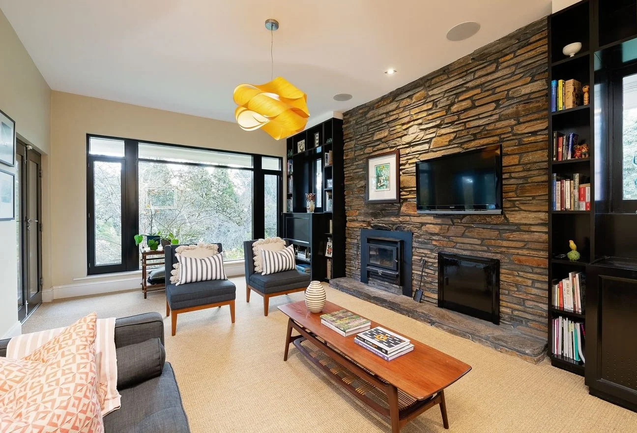 Living room with stone accent wall, mounted flat-screen TV, black bookshelves, and beige carpeted floor.