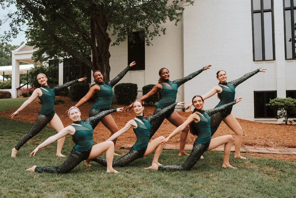Six teens in one-legged green costumes posing outside in the grass
