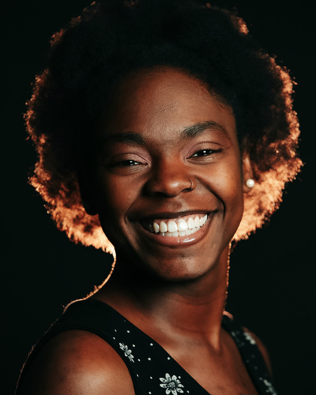 Dark skin woman smiling brightly in front of a black background