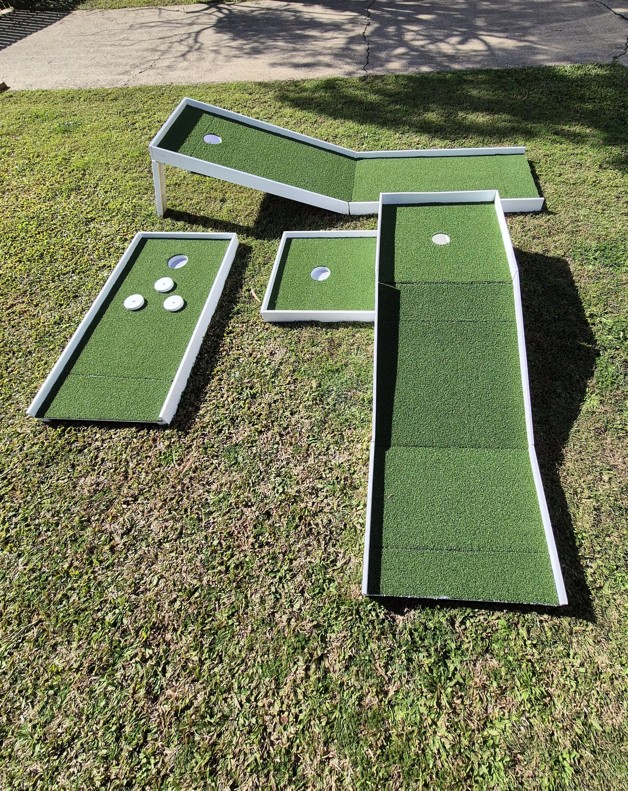 Assembled mini golf game with green turf on white-framed boards arranged on grass.