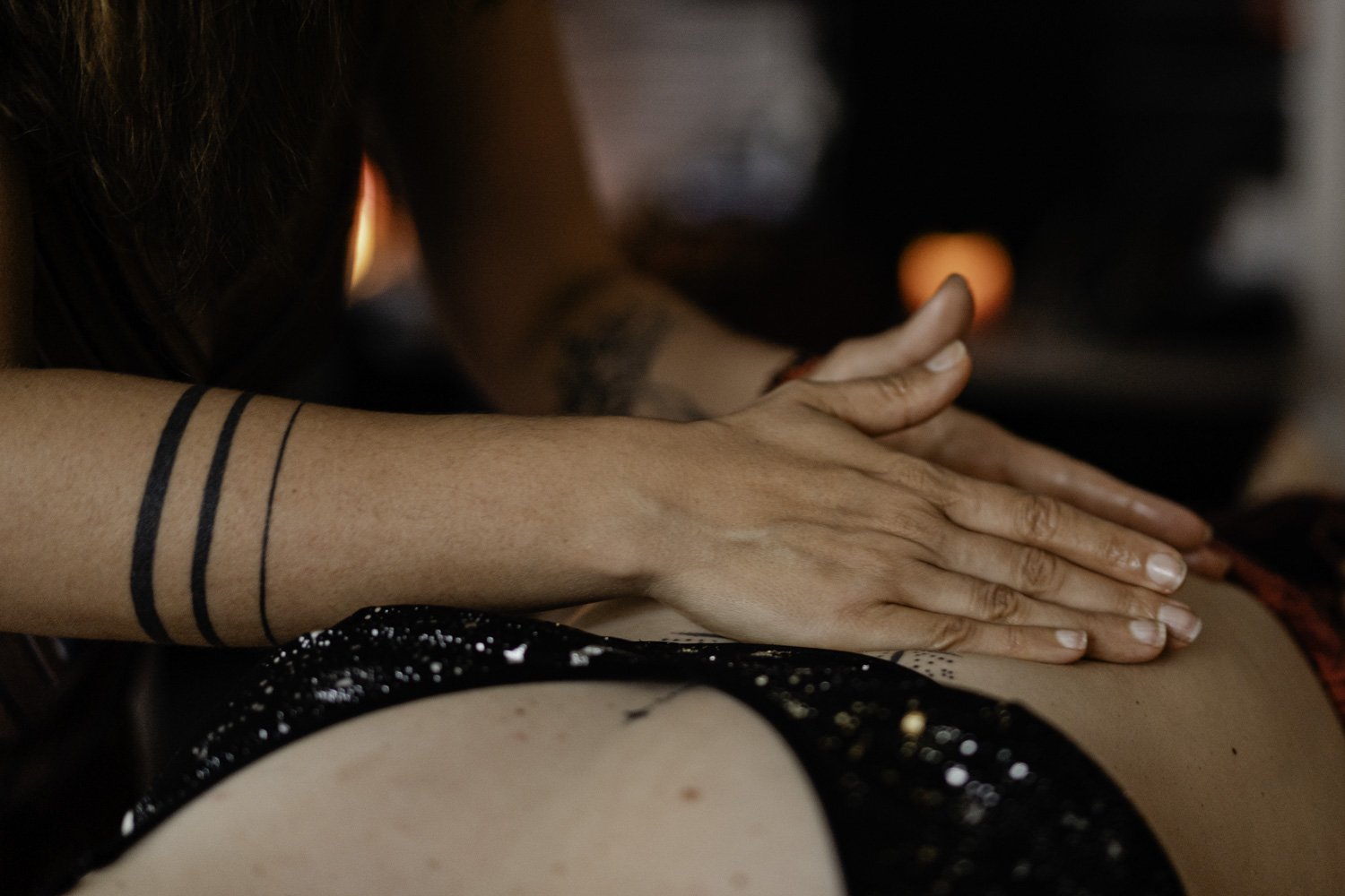 Mains faisant un massage sur un dos, avec des tatouages visibles sur les bras.