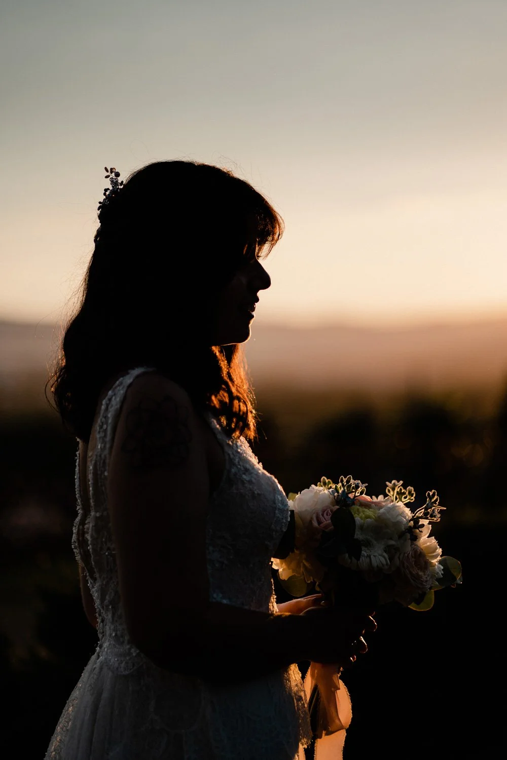 Silhouette d'une femme en robe blanche tenant un bouquet de fleurs lors d'un coucher de soleil.
