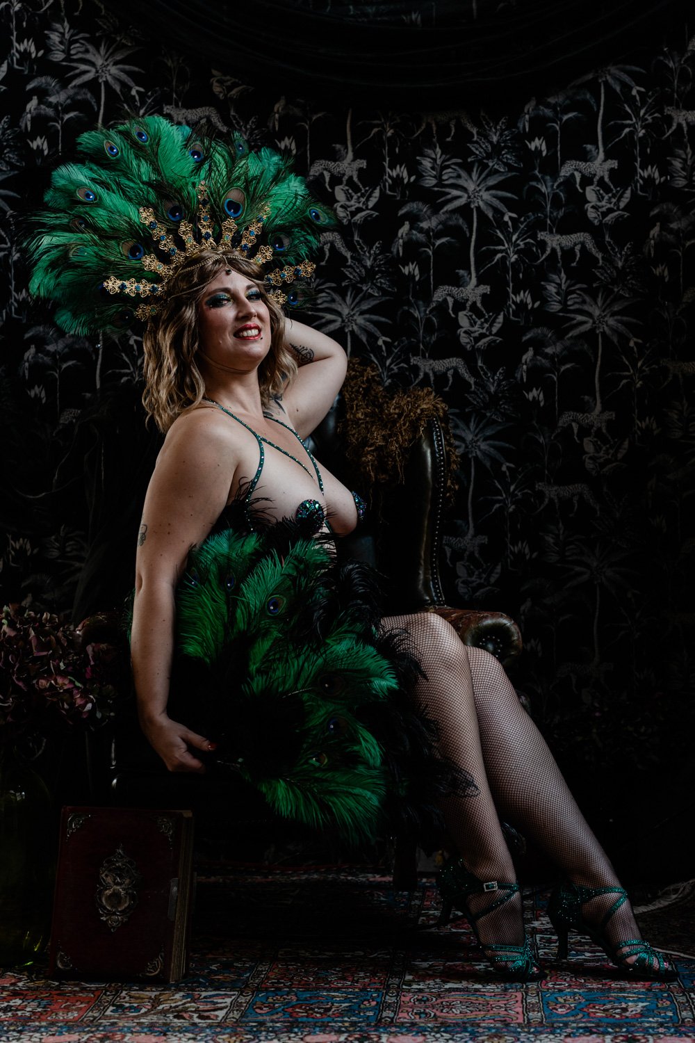 Personne en costume à plumes vertes assise sur une chaise, fond exotique.