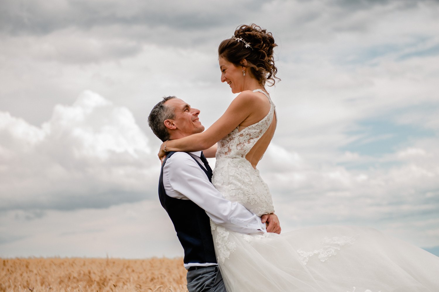 Couple marié s'embrassant dans un champ sous un ciel nuageux.