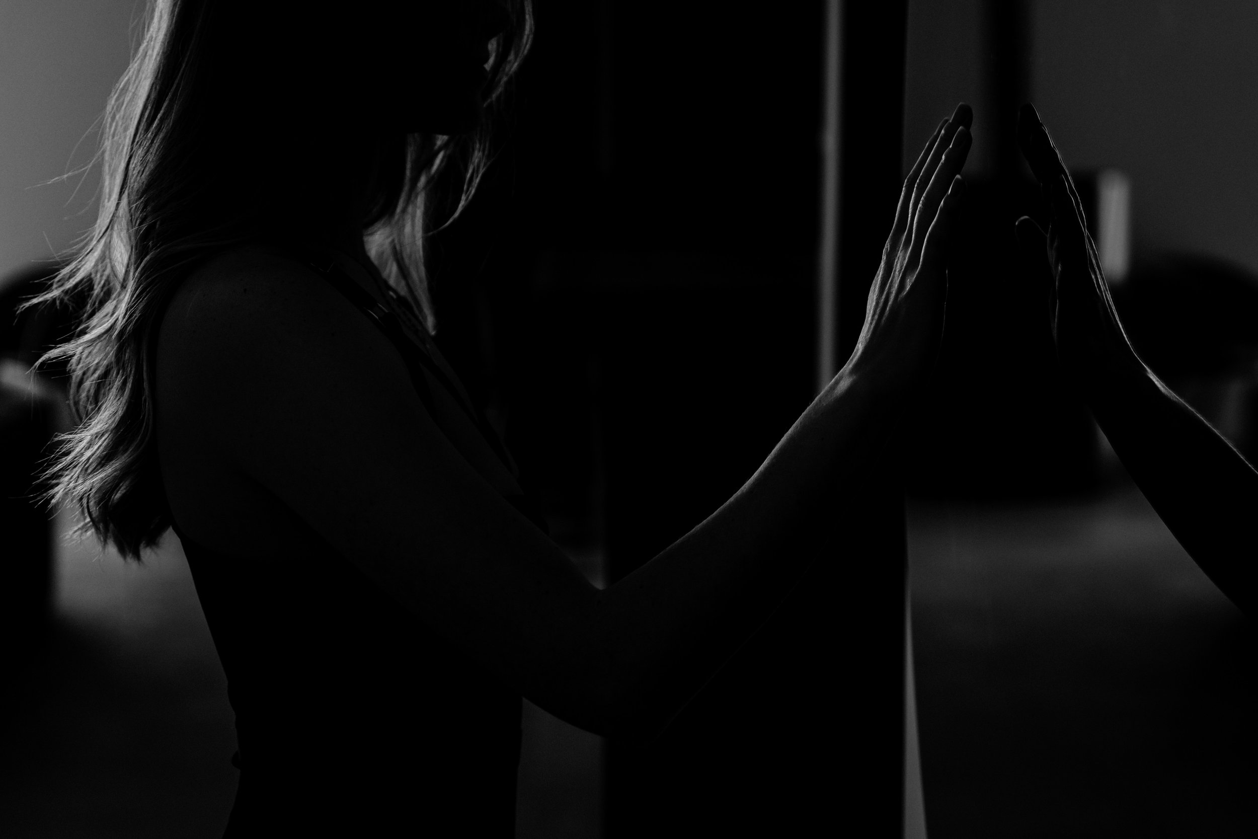 Silhouette d'une femme touchant un miroir, reflet des mains visibles, en noir et blanc.