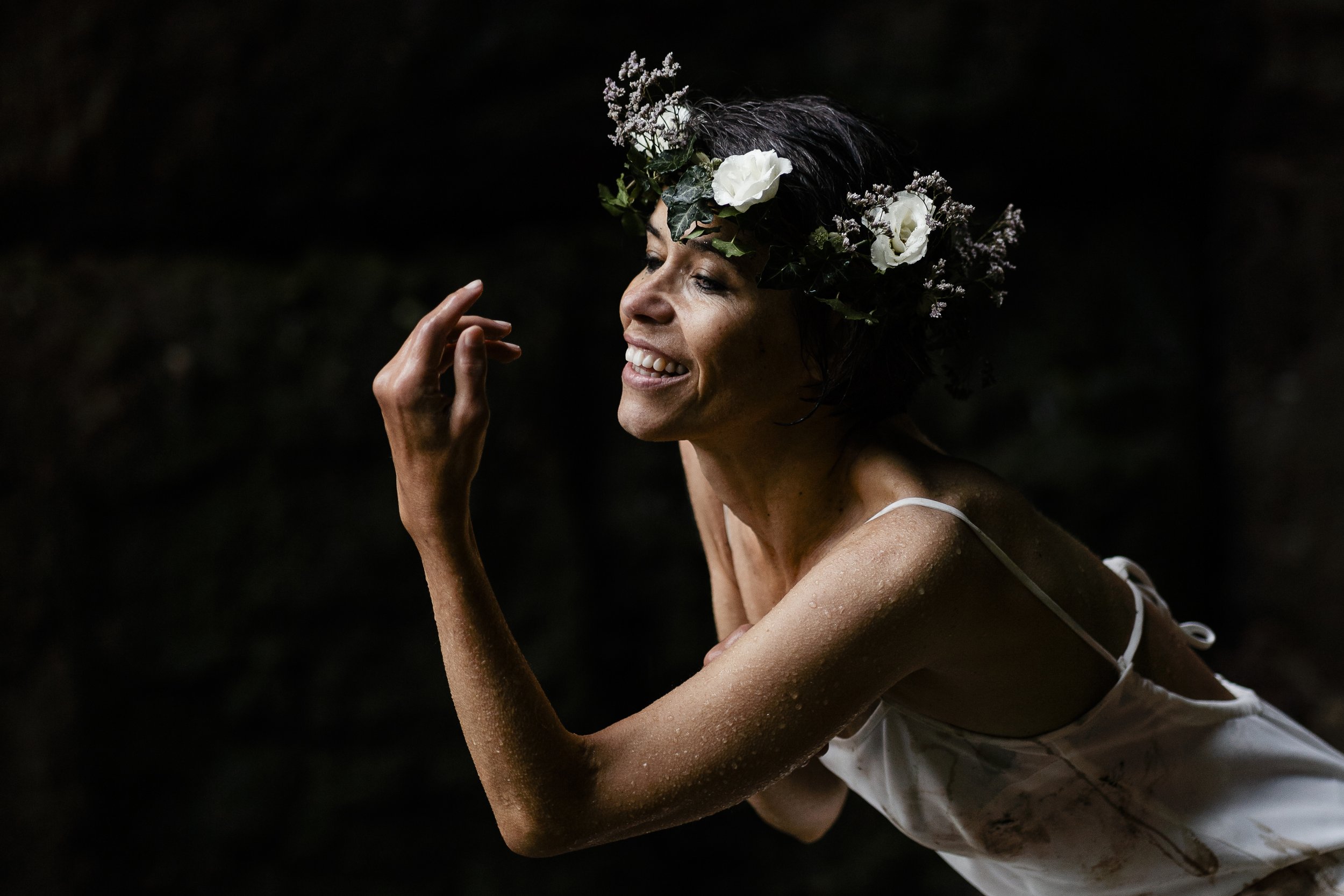 Femme souriante portant une couronne de fleurs blanches. Elle est habillée d'une robe blanche et a la peau légèrement humide.