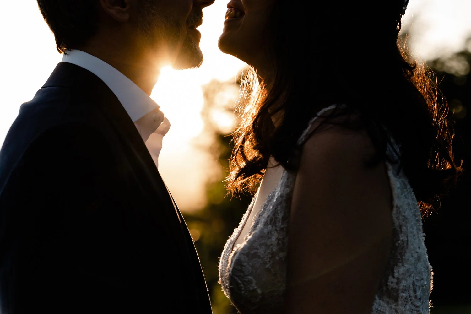 Un couple de mariage en silhouette, se tenant face à face avec le soleil couchant en arrière-plan.