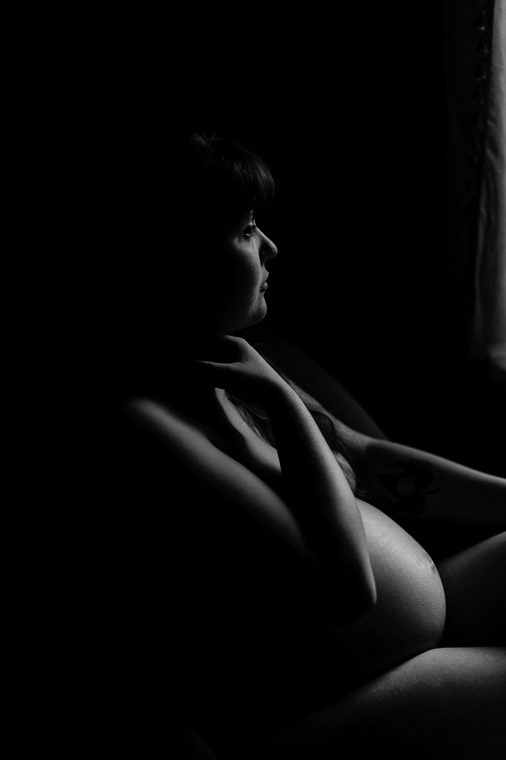 Silhouette en noir et blanc d'une femme enceinte regardant par la fenêtre.