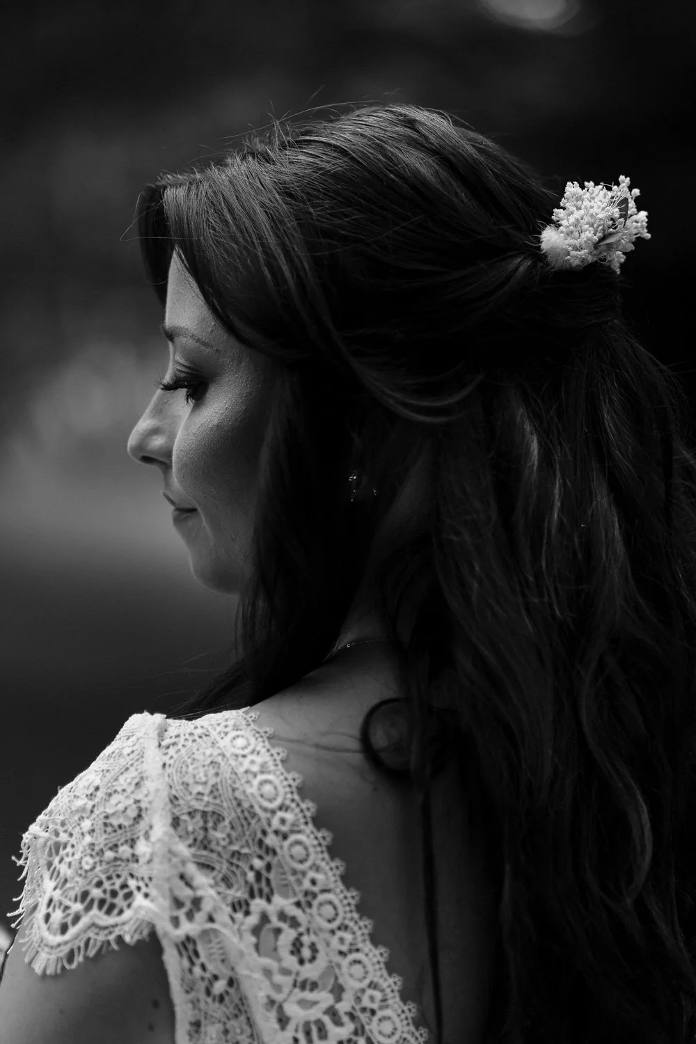 Portrait en noir et blanc d'une femme vue de profil, portant une robe en dentelle et une chevelure longue avec une fleur à l'arrière de la tête.