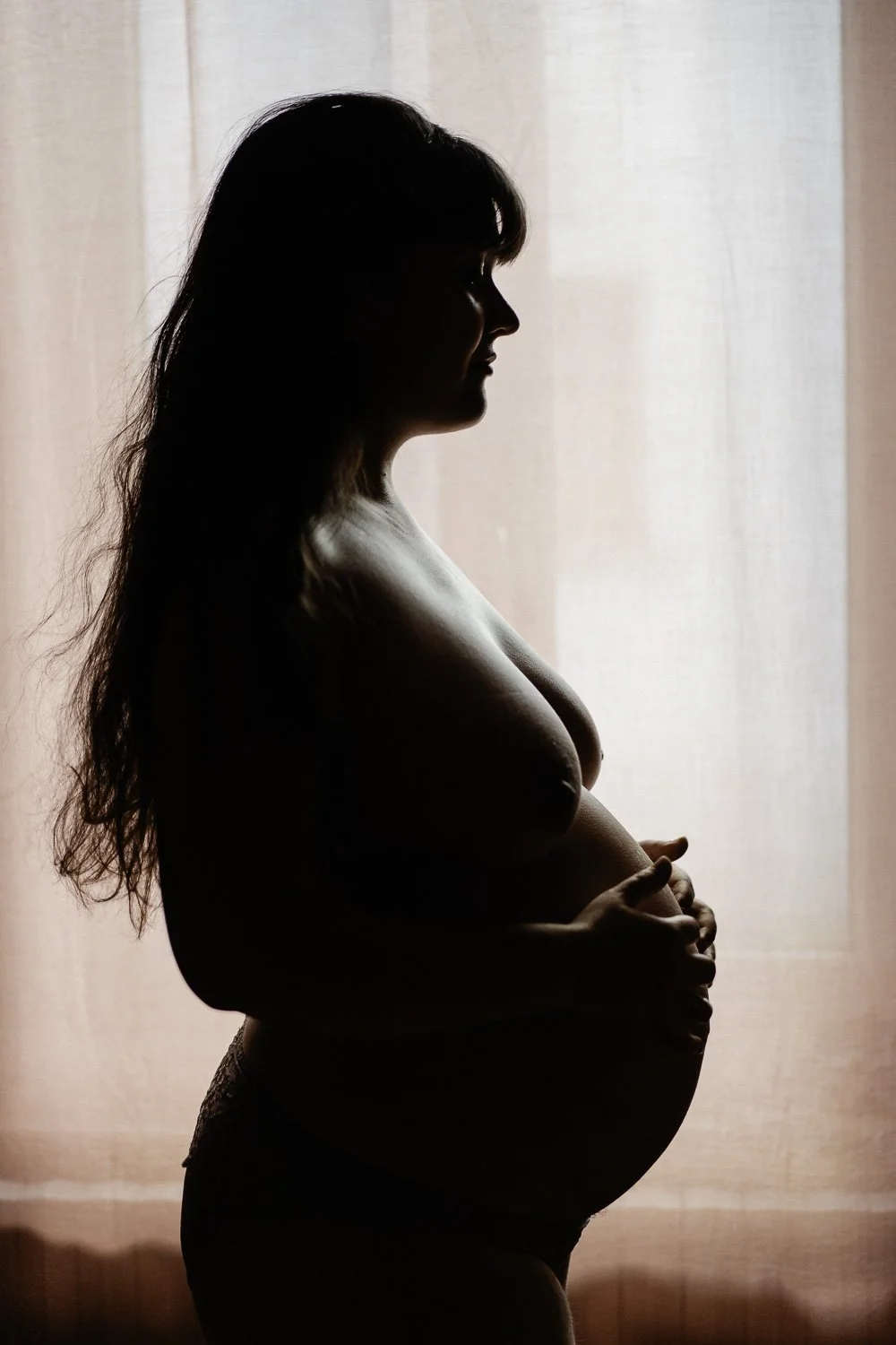 Silhouette d'une femme enceinte vue de profil devant un rideau lumineux