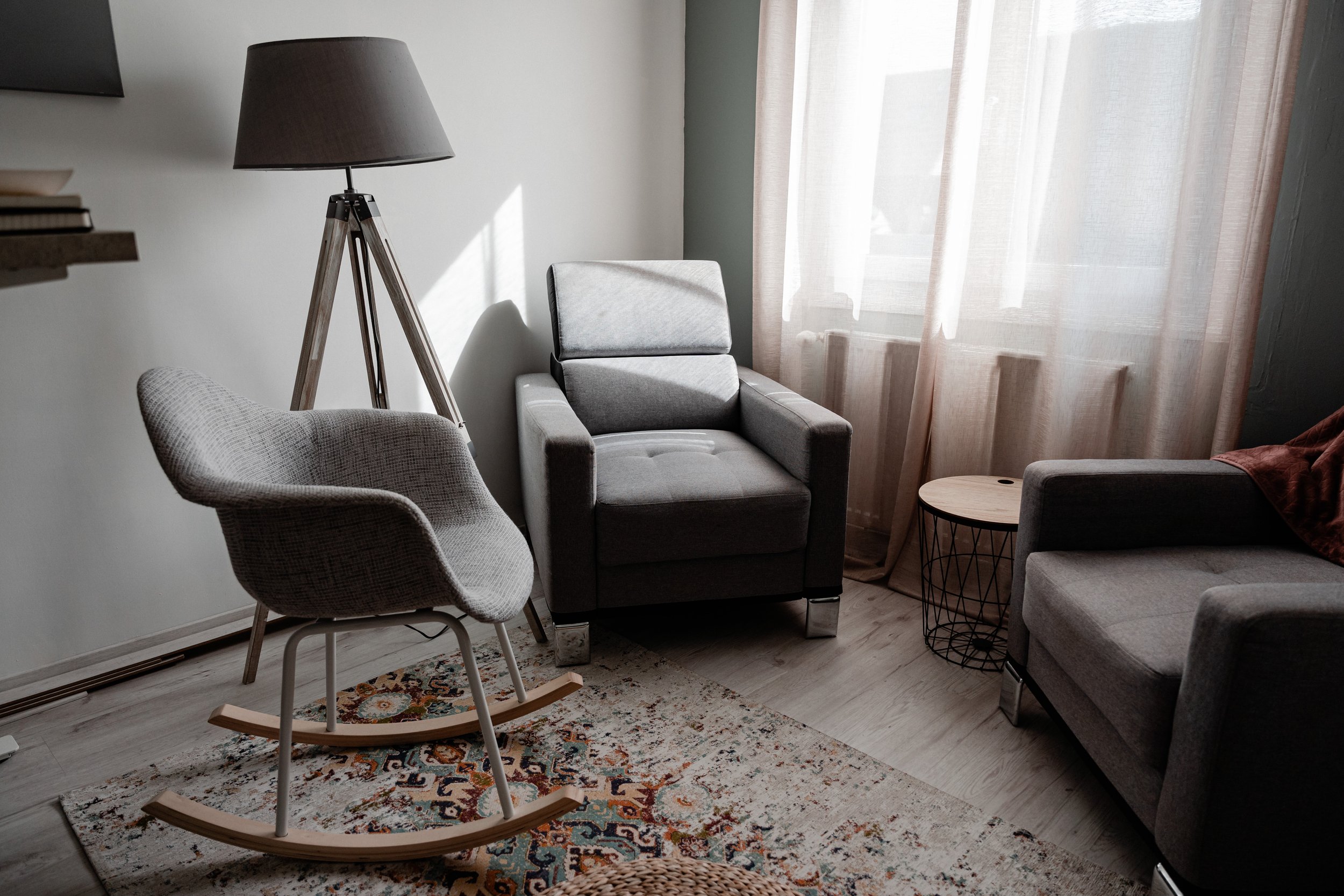 Salon moderne avec fauteuils gris, lampe sur trépied, chaise berçante et petite table en bois.