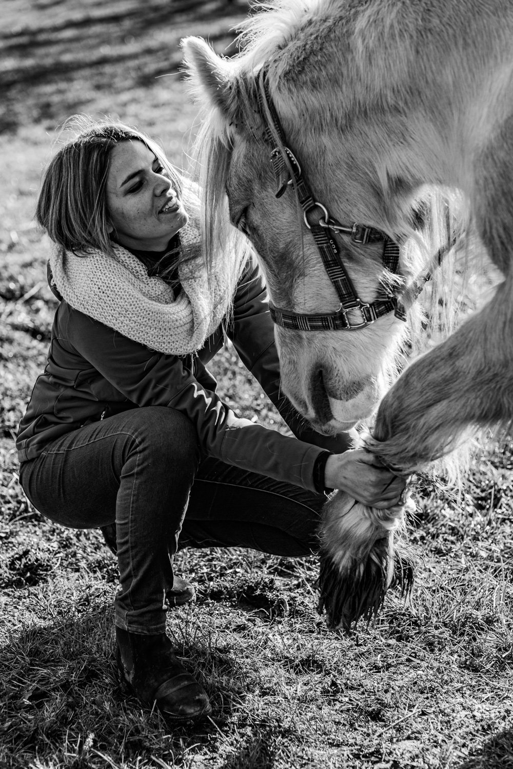 Une femme sourit en caressant un cheval dans un champ.