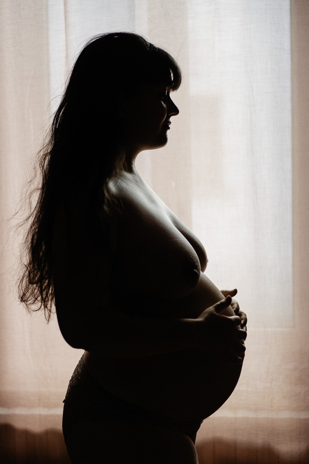 Silhouette d'une femme enceinte devant une fenêtre, tenant son ventre.