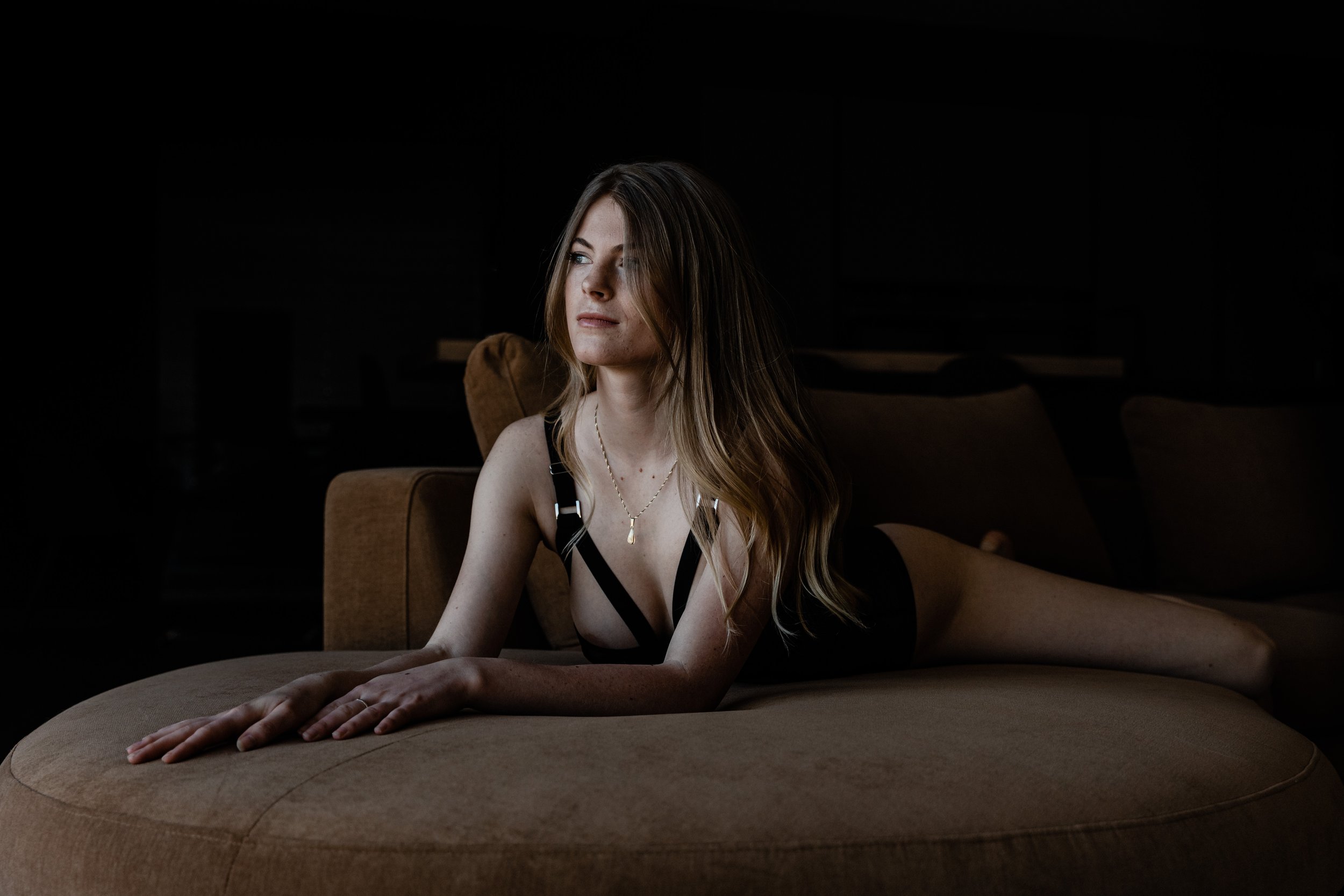 Femme allongée sur un canapé beige dans une pièce sombre, vêtue d'une tenue noire.