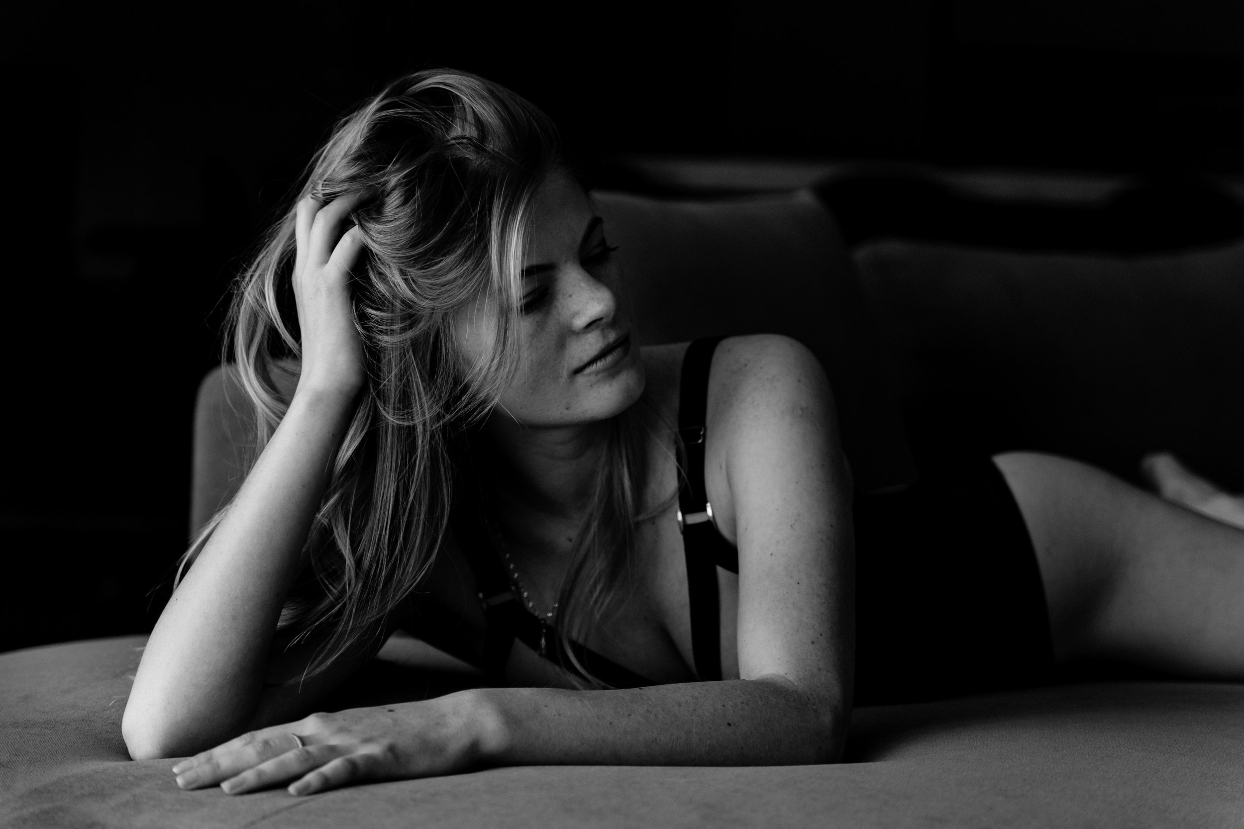 Femme allongée sur un canapé, tenant ses cheveux, en noir et blanc.