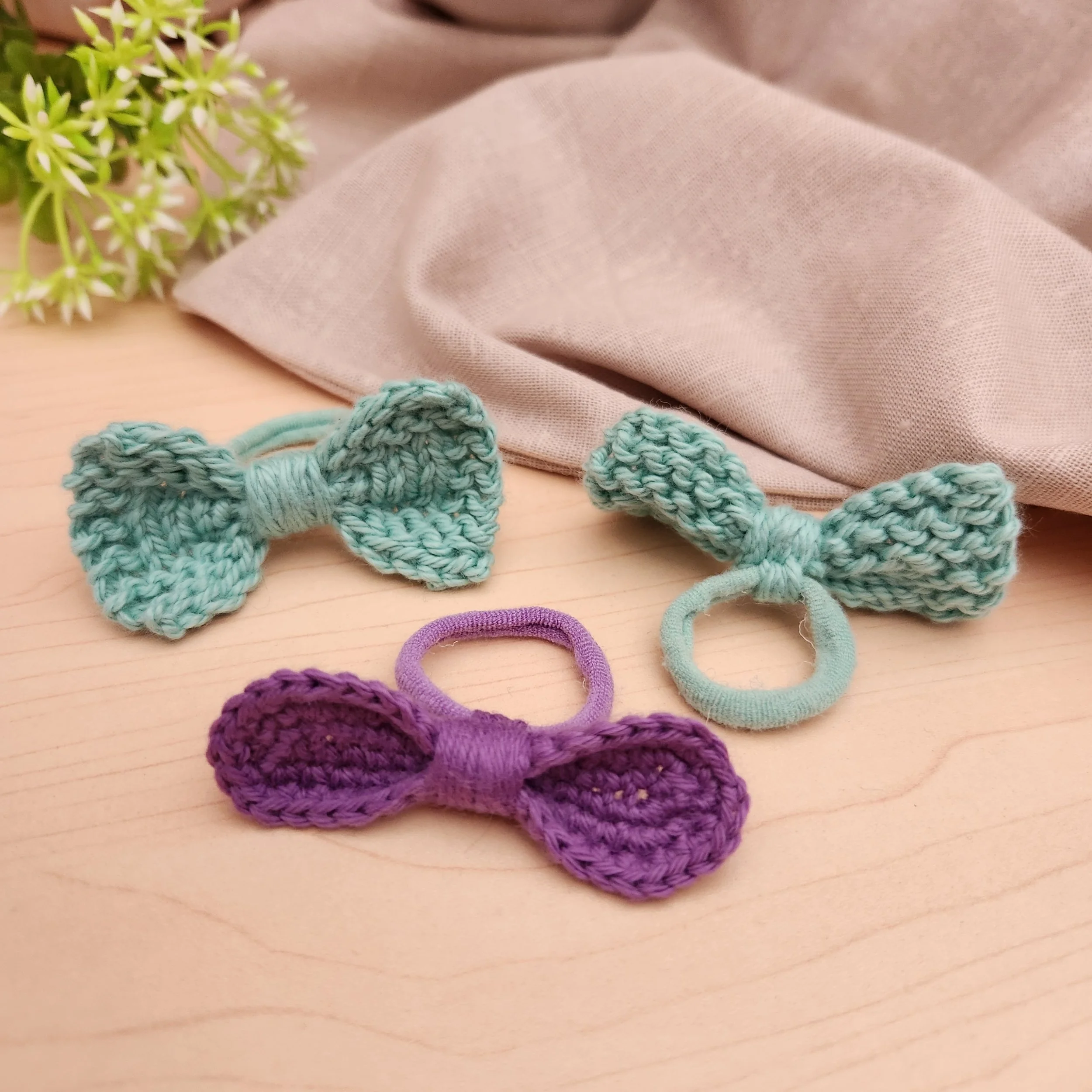 One crochet and two knitted hair bows made from cotton yarn, with one showing the back to display how the hair tie is secured.