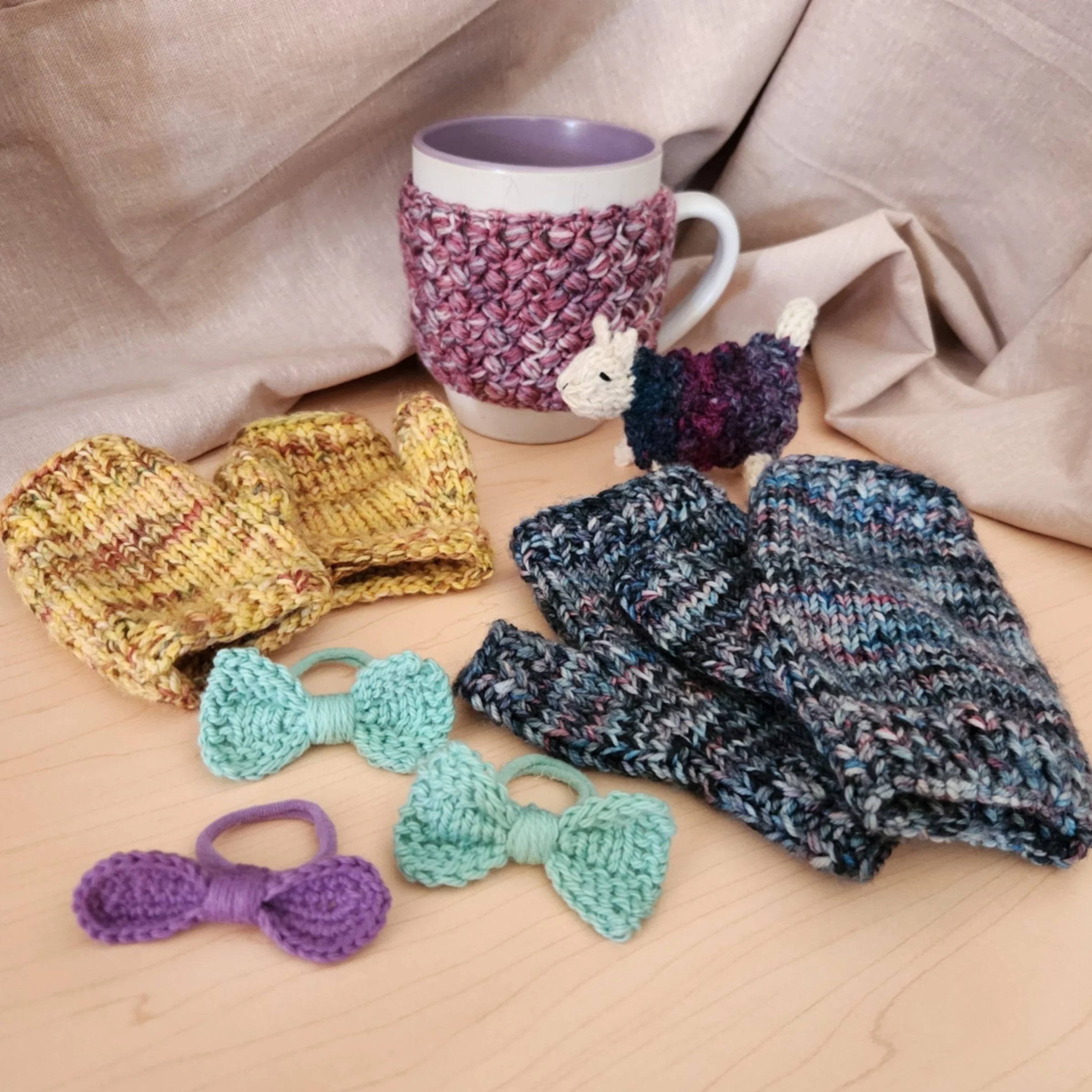 Four handmade knit and crochet winter projects: fingerless mitts, a crochet mug cosy, two bow hair ties (knit and crochet), and a mini knitted sheep made from handspun yarn.