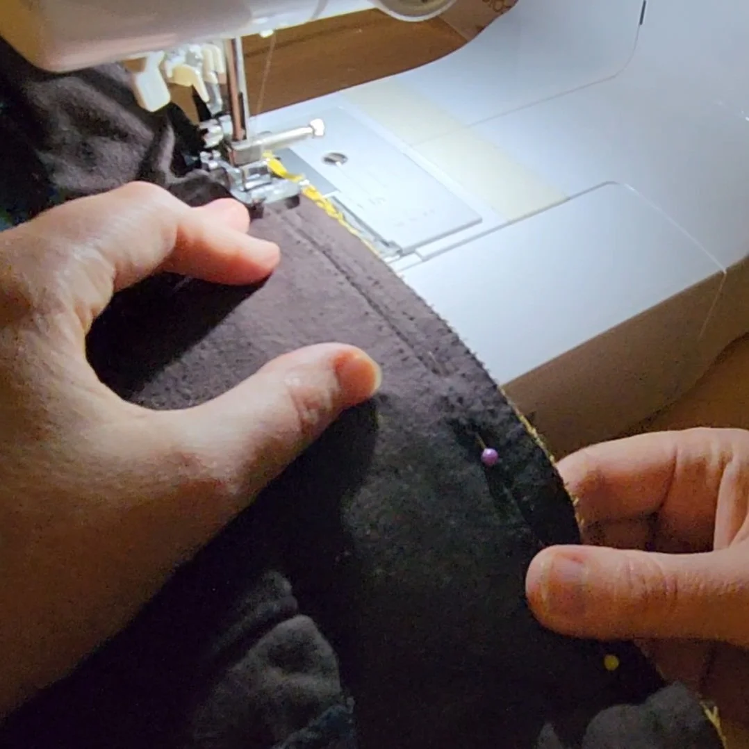 Close-up of a sewing machine stitching a gusset panel into the side seam of brown corduroy pants.