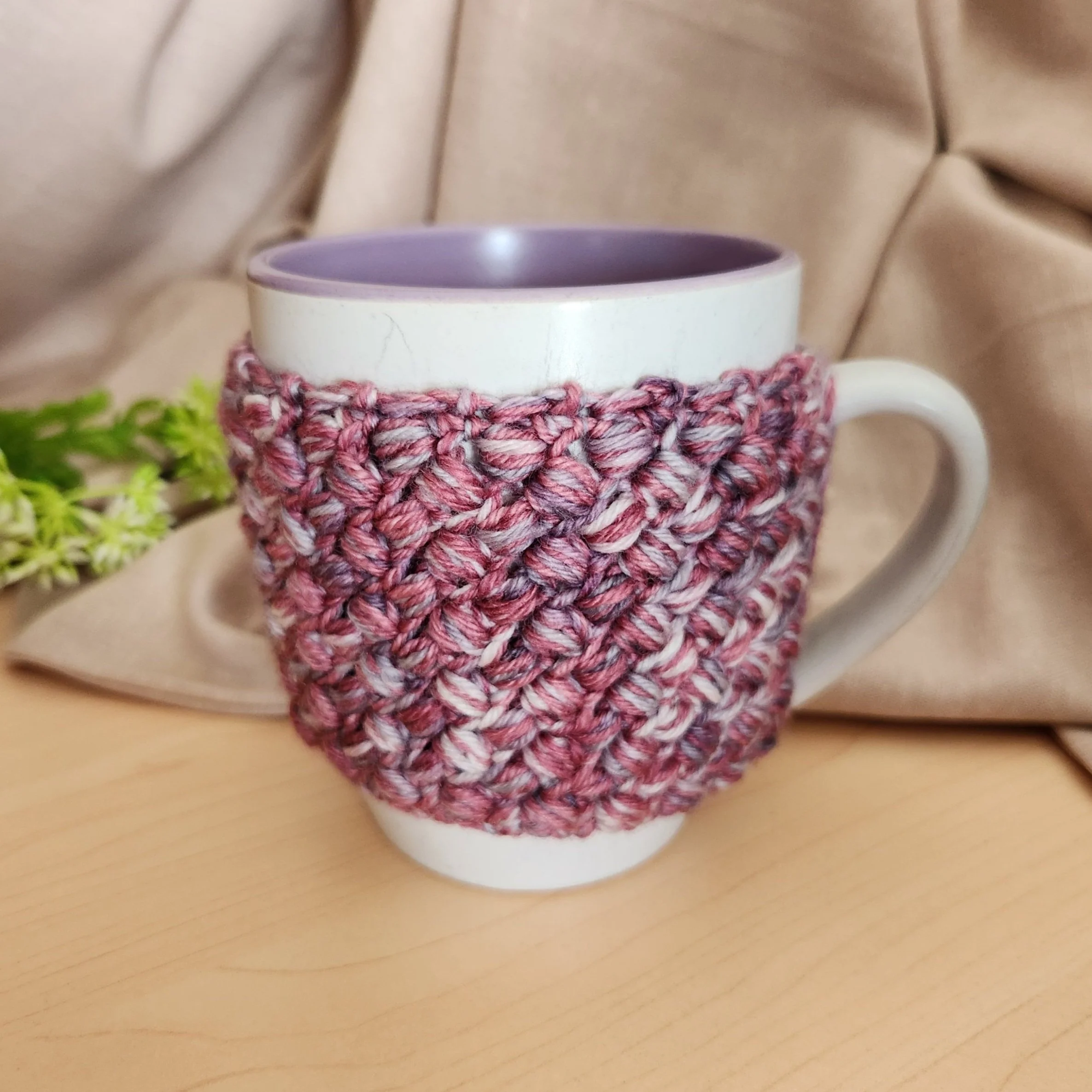 Crocheted mug cosy made with scrap sock yarn in a marled violet and pink, styled on a ceramic mug for winter.