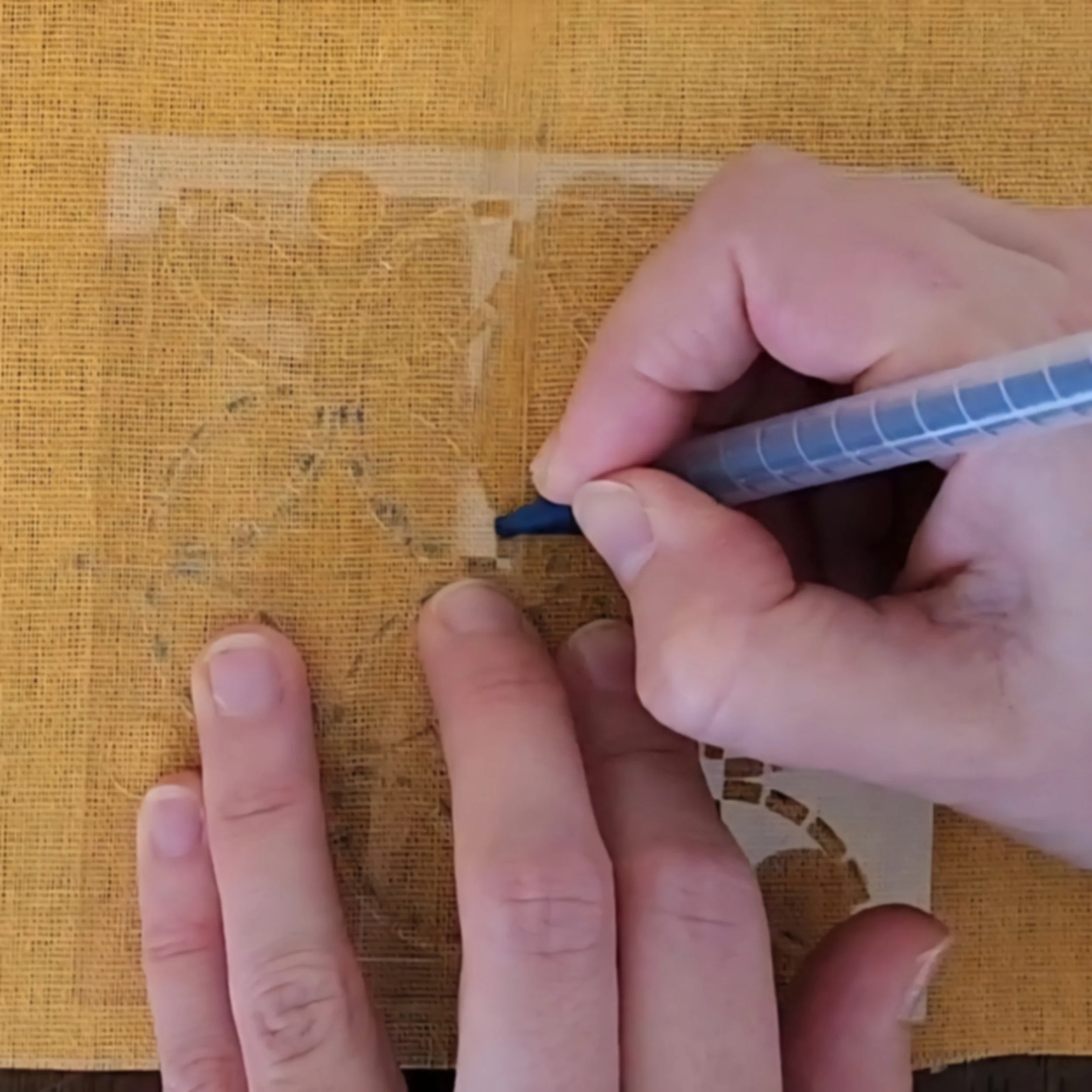 Close-up of mustard linen fabric with sashiko stencil and blue washable tailor’s pencil drawing the design.