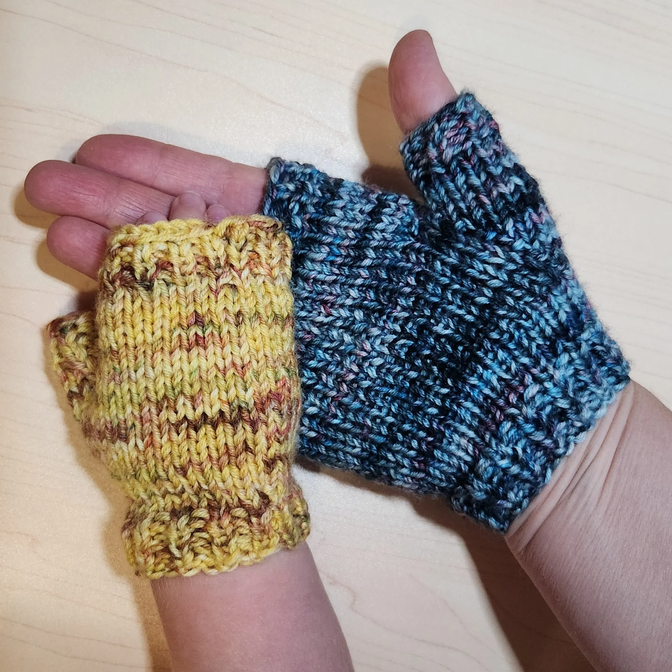 My hand and my toddler’s hand wearing matching fingerless mitts, knit from scrap hand-dyed yarn.