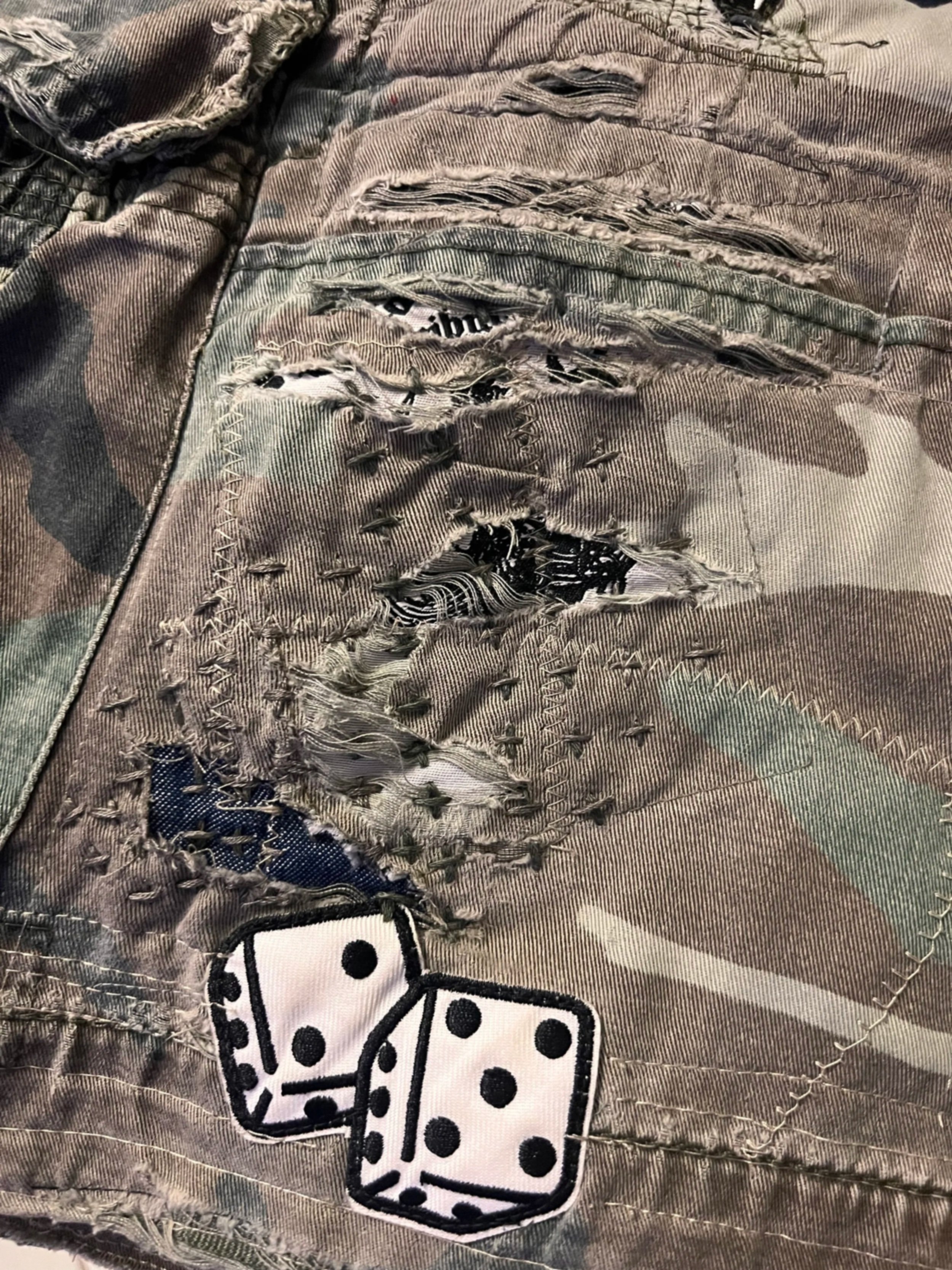Close-up of camo cargo shorts with sashiko mending stitches and a dice patch.