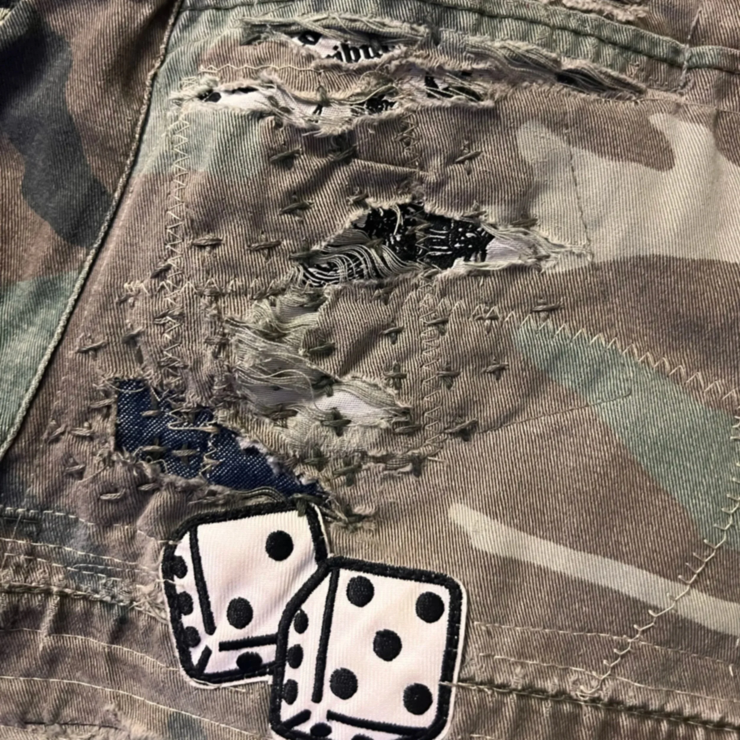 Detailed view of torn camo shorts repaired with sashiko stitching around a dice patch.