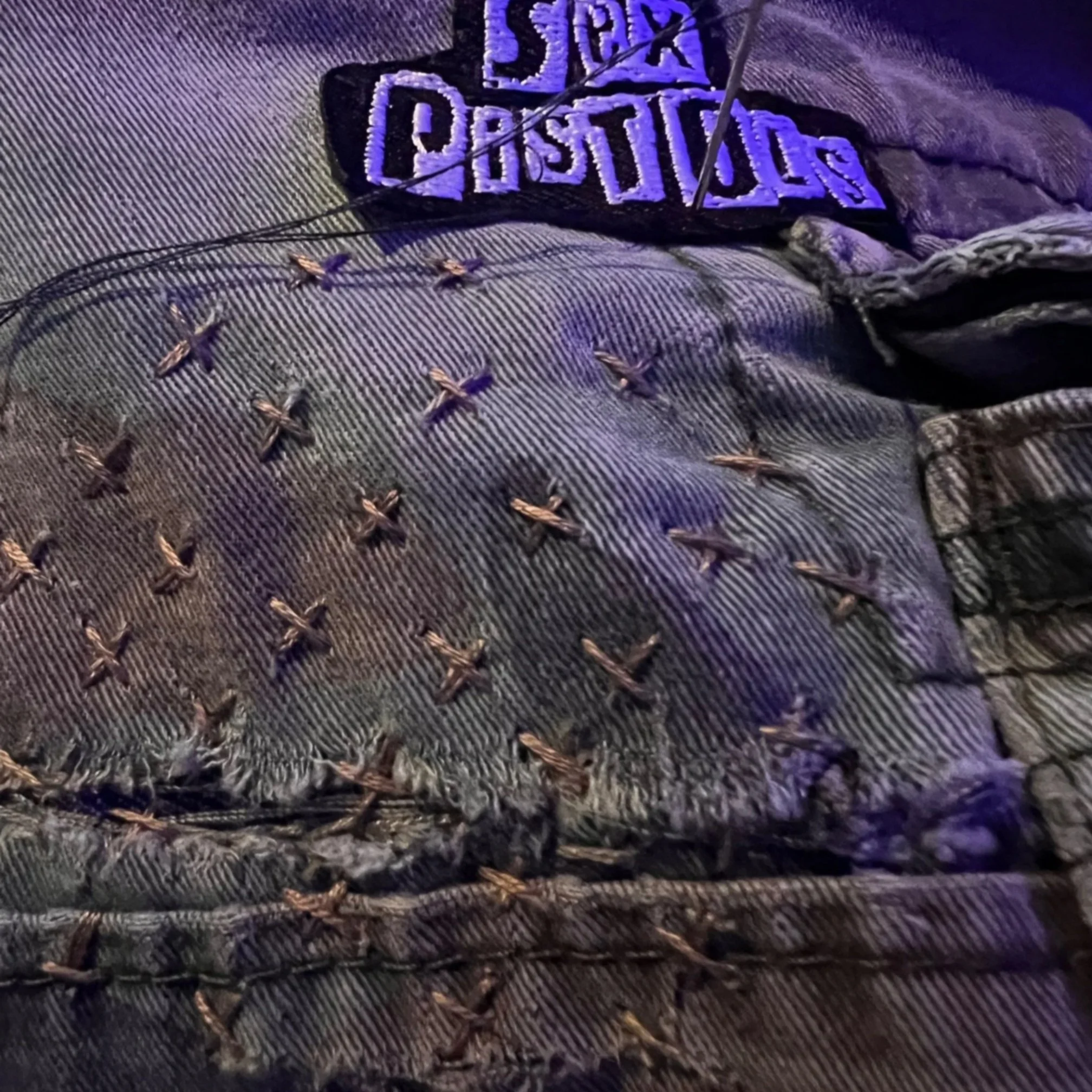 Close-up of sashiko cross stitches on camo shorts with a Sex Pistols patch.