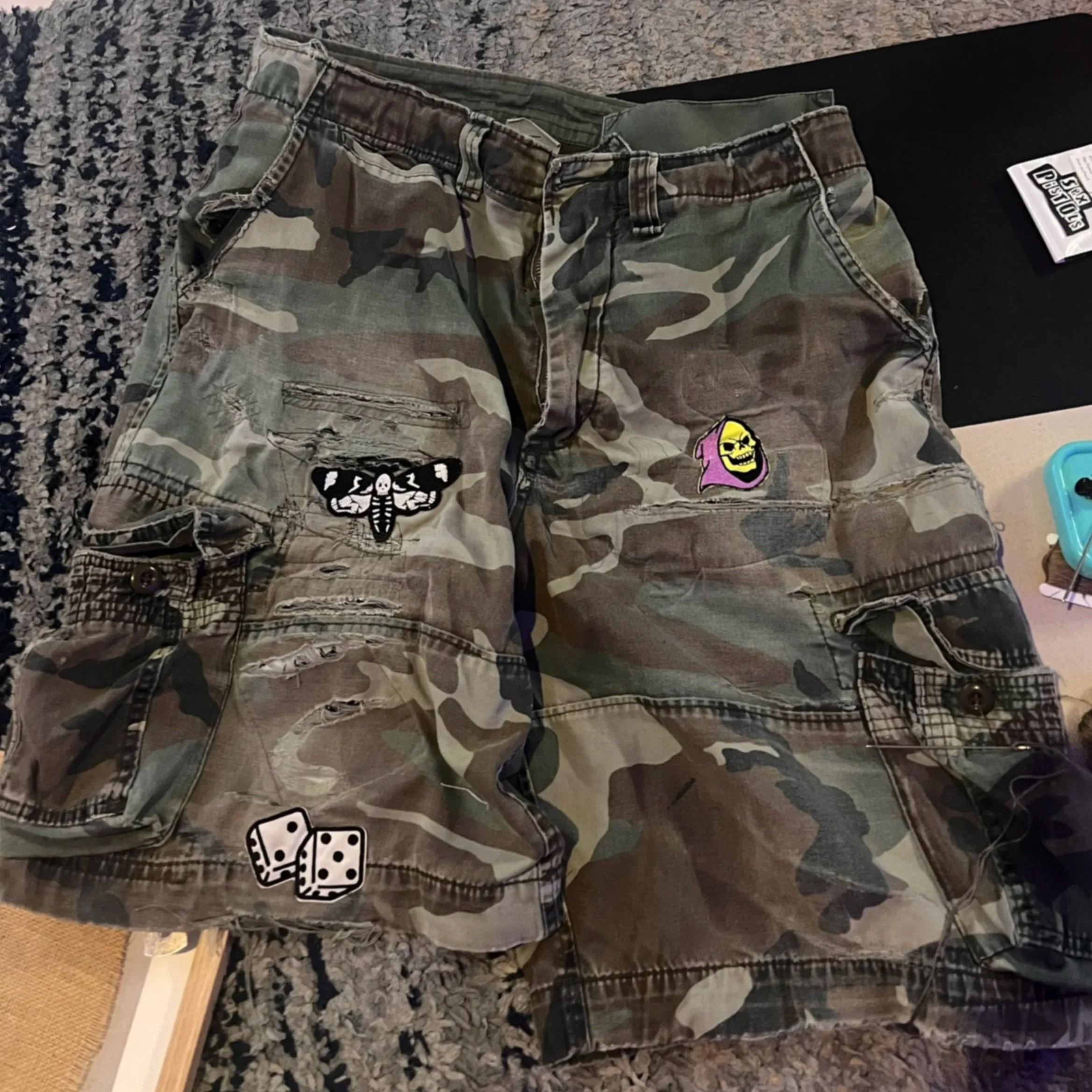 Camo cargo shorts laid flat showing worn areas and holes before sashiko mending.