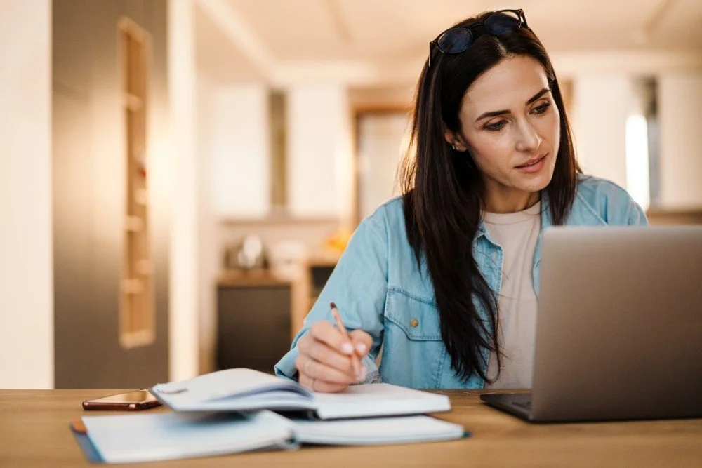 Woman making notes in diary looking at laptop