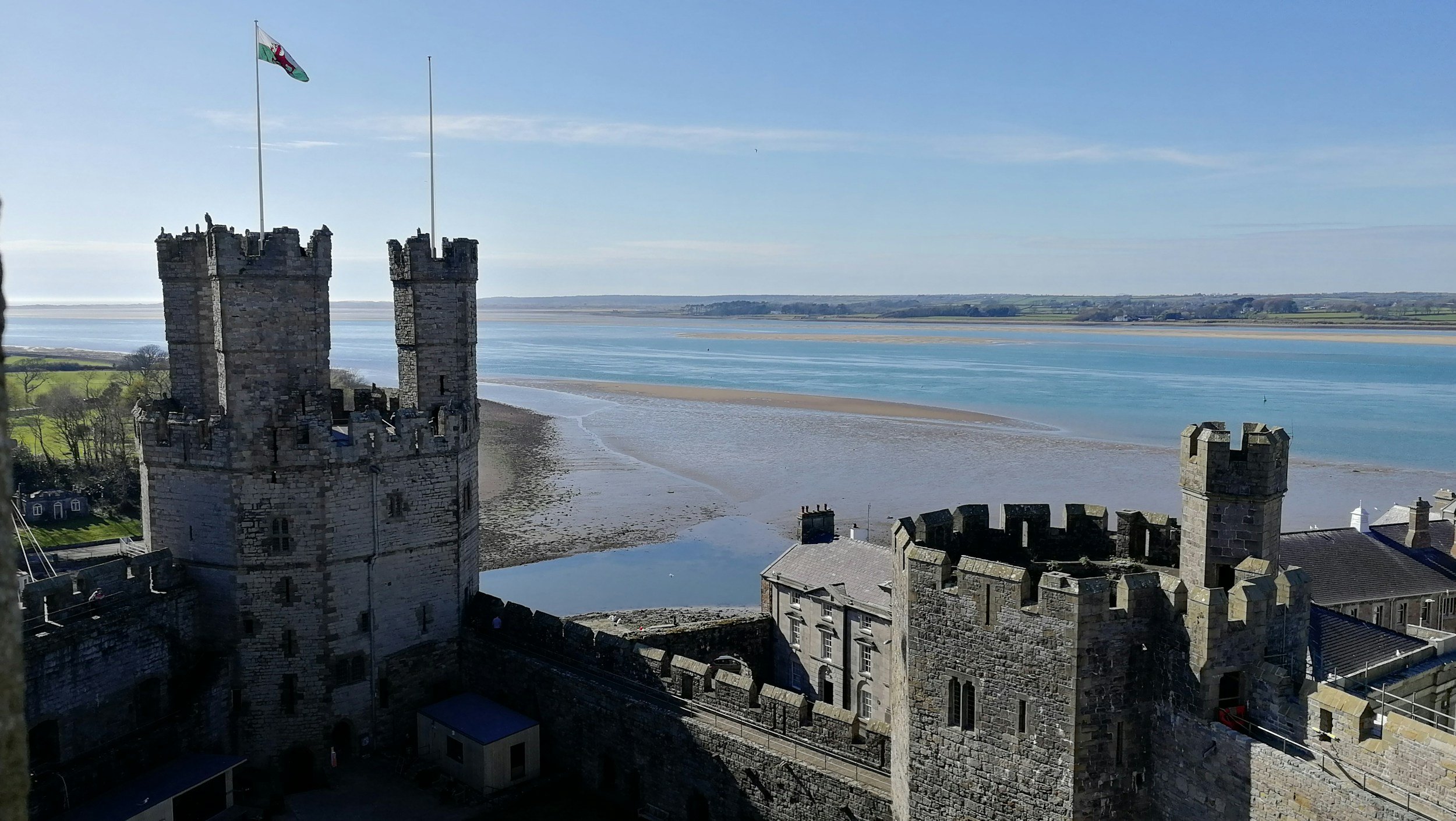 View of a historic stone castle overlooking a wide river under a blue sky.