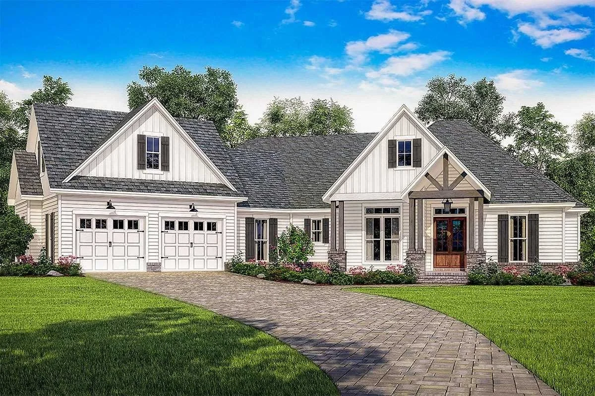 A modern white house with black shutters, a gray shingle roof, a brick front porch, and a curved stone driveway surrounded by green grass and trees.