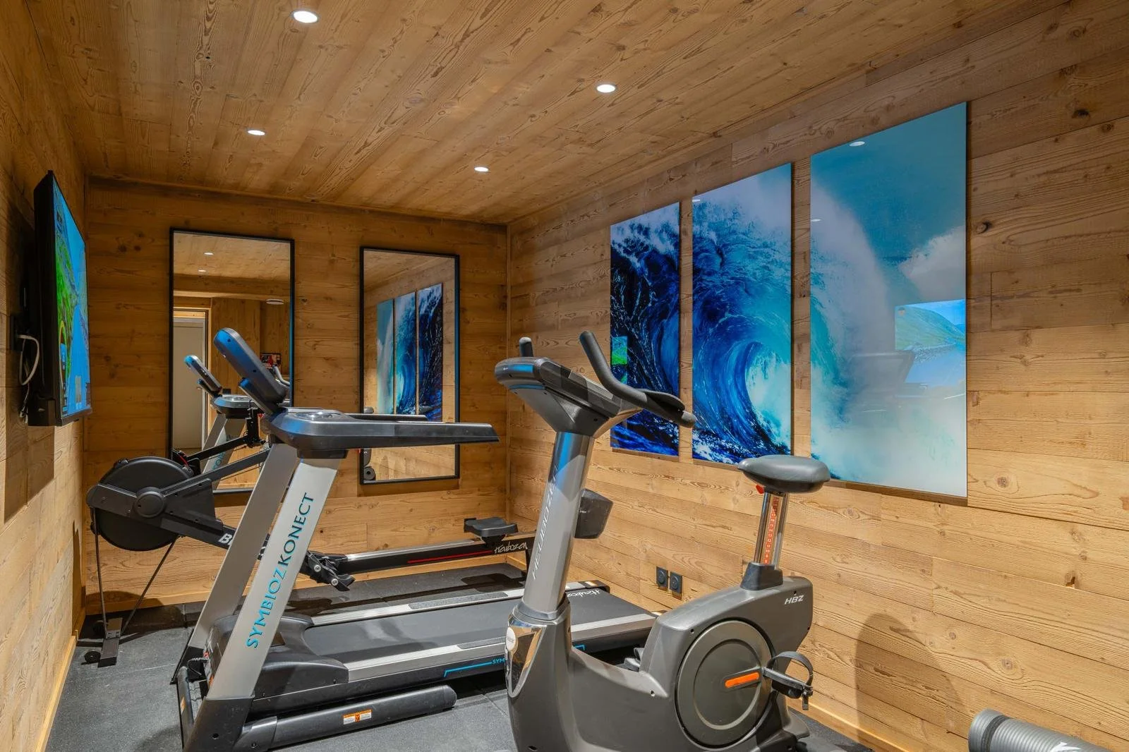 Home gym with treadmill and stationary bike in a wooden room with three large ocean wave paintings