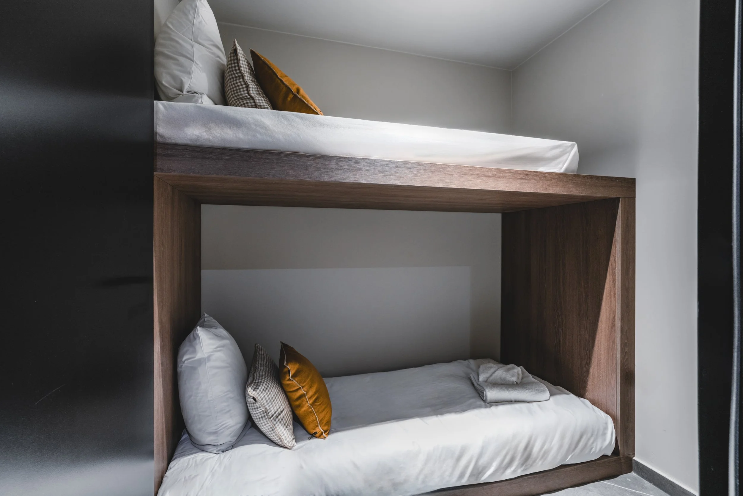 Bunk beds with white bedding, pillows, and folded towels in a small room with gray walls.