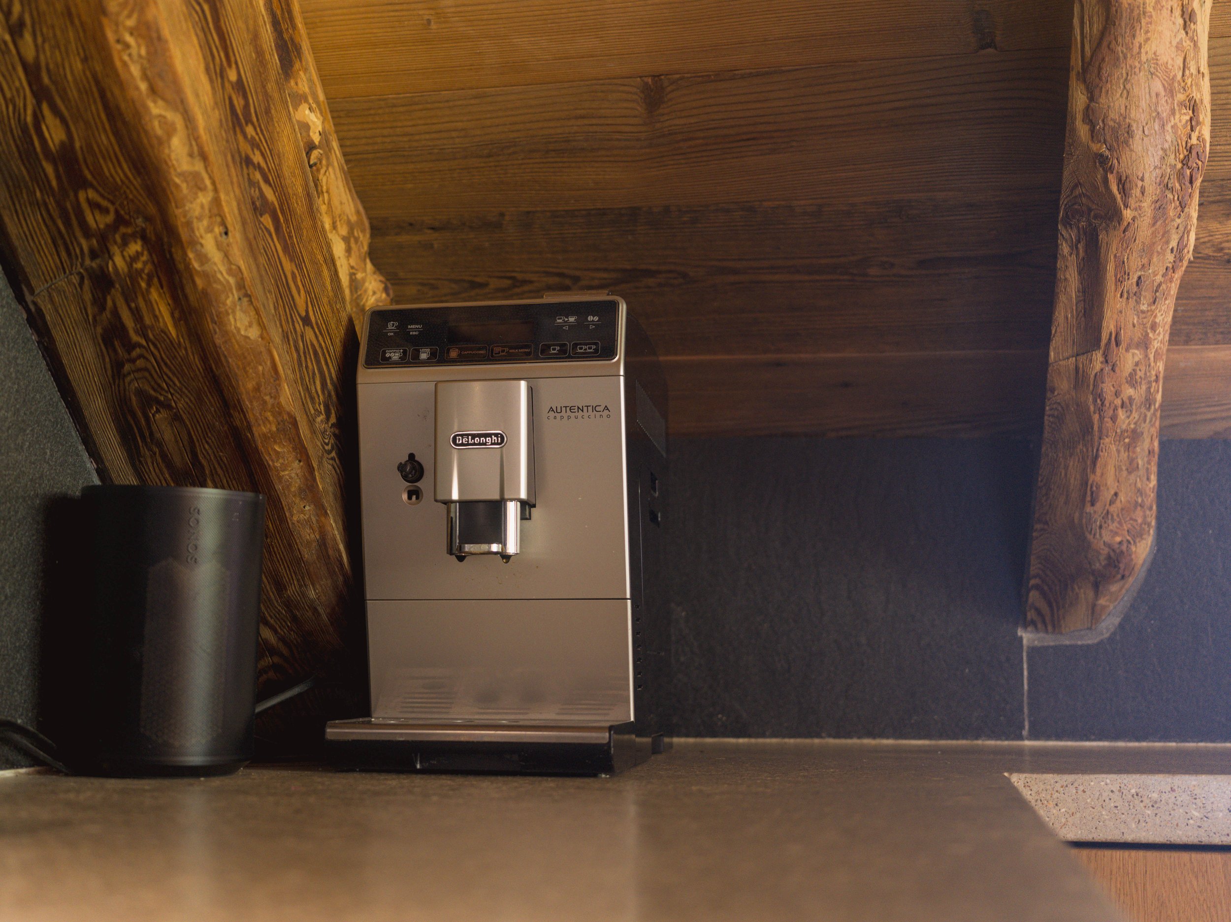 Une machine à café, une tasse noire et un meuble d'angle en bois dans un décor chaleureux et rustique.