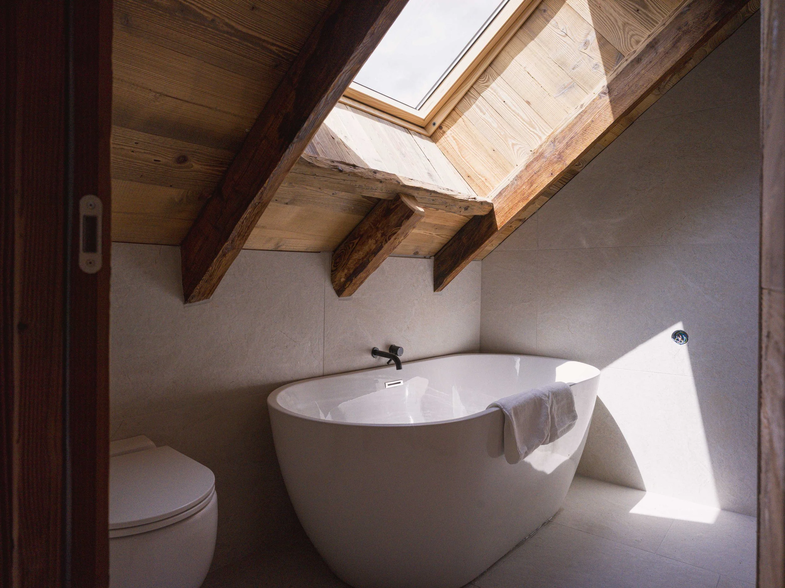 Une salle de bains équipée d'une baignoire, de toilettes et d'une lucarne au plafond.