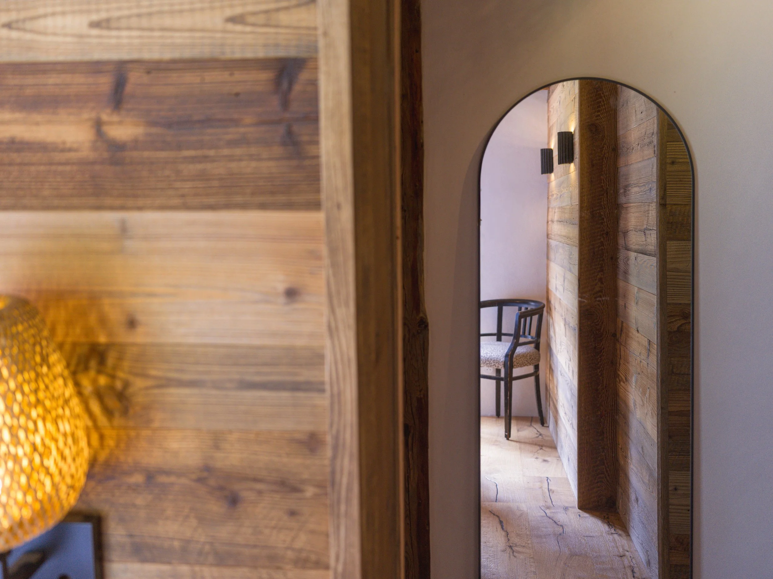 Intérieur d'une pièce avec un sol, des murs et des meubles en bois, dont une chaise. La photo a été prise à travers une ouverture circulaire pratiquée dans une cloison en bois.