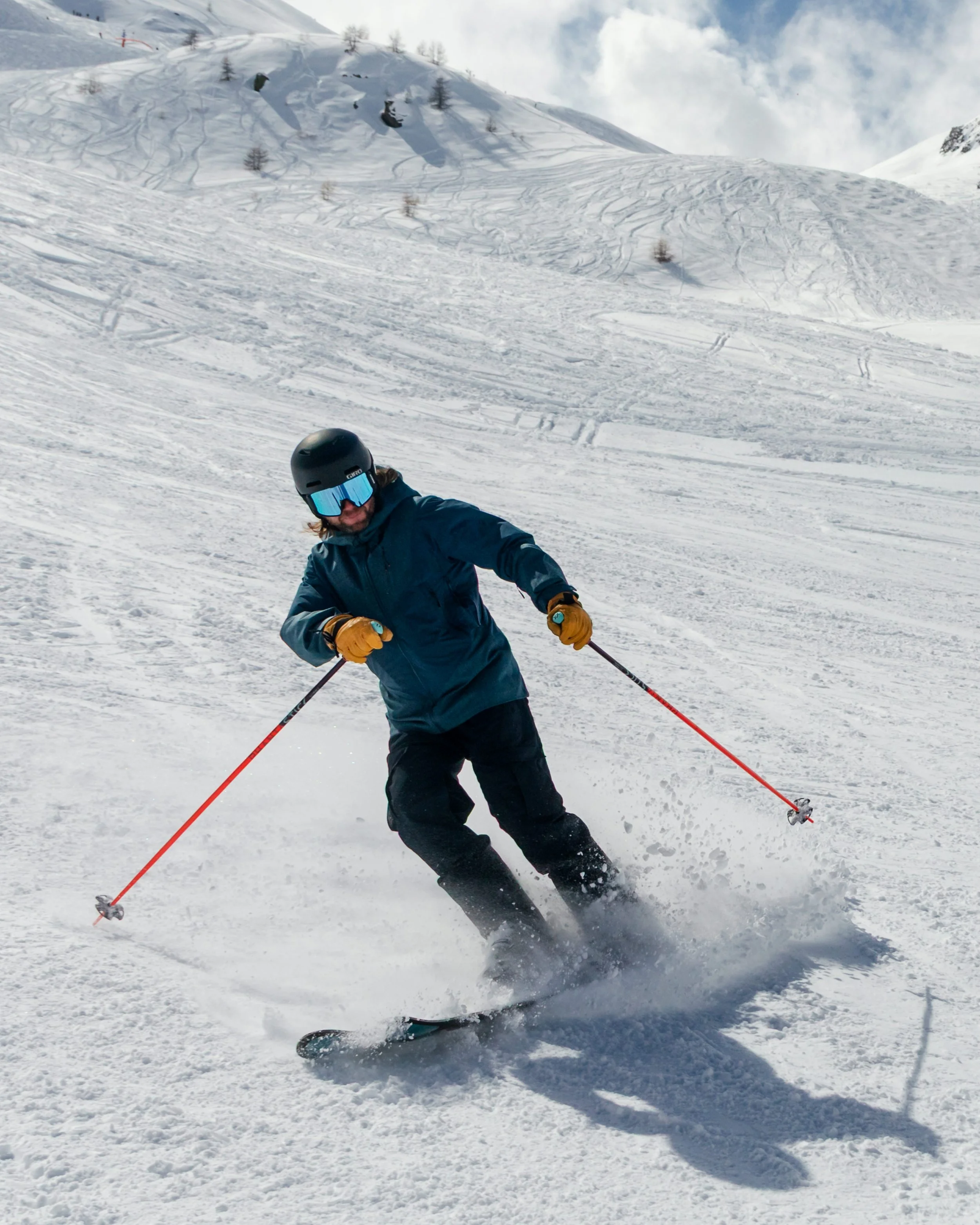 A person skiing on a snowy mountain slope, wearing a black helmet, blue goggles, a blue jacket, black pants, and yellow gloves.