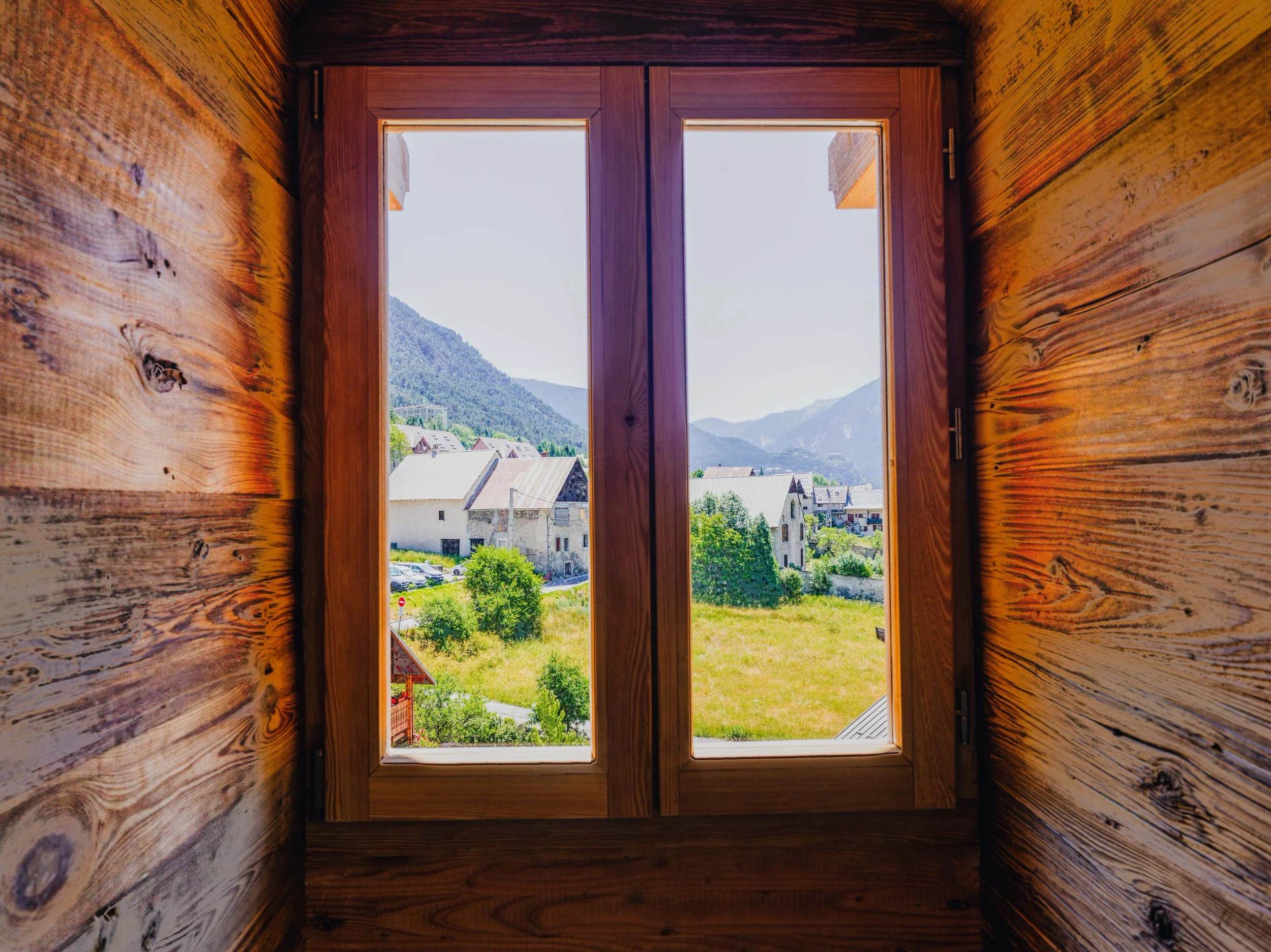 Wooden interior wall with a window showing a scenic mountain view and houses outside.