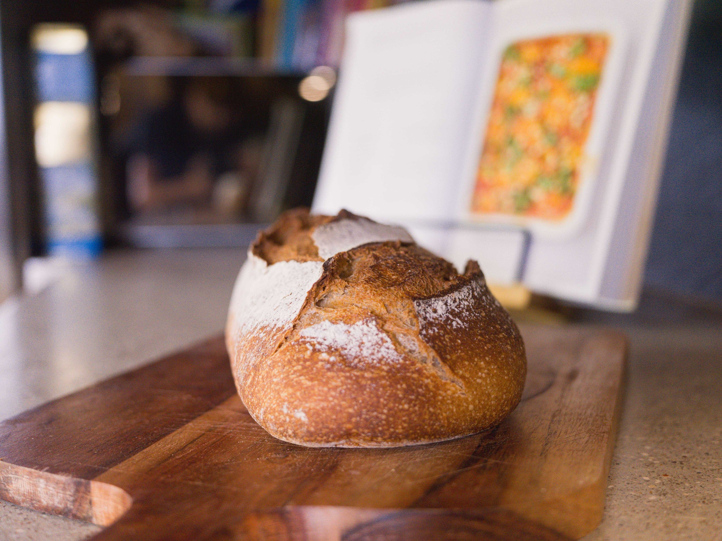 Une miche de pain rustique à la croûte croustillante et saupoudrée de farine, posée sur une planche à découper en bois.