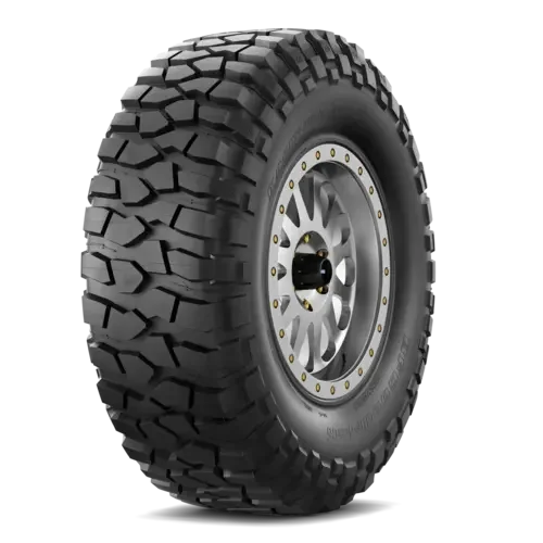 A large off-road vehicle tire with deep treads mounted on a silver alloy wheel.