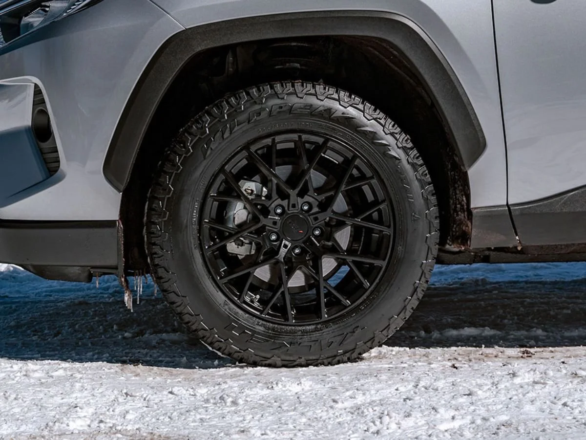 Falken Wildpeak A/T tire on a black mesh wheel parked on snow, showing aggressive all-terrain tread.