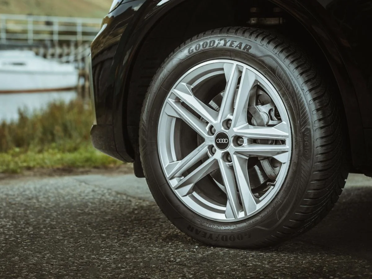 Goodyear Vector all-season tire mounted on a silver Audi alloy wheel parked near a harbor.