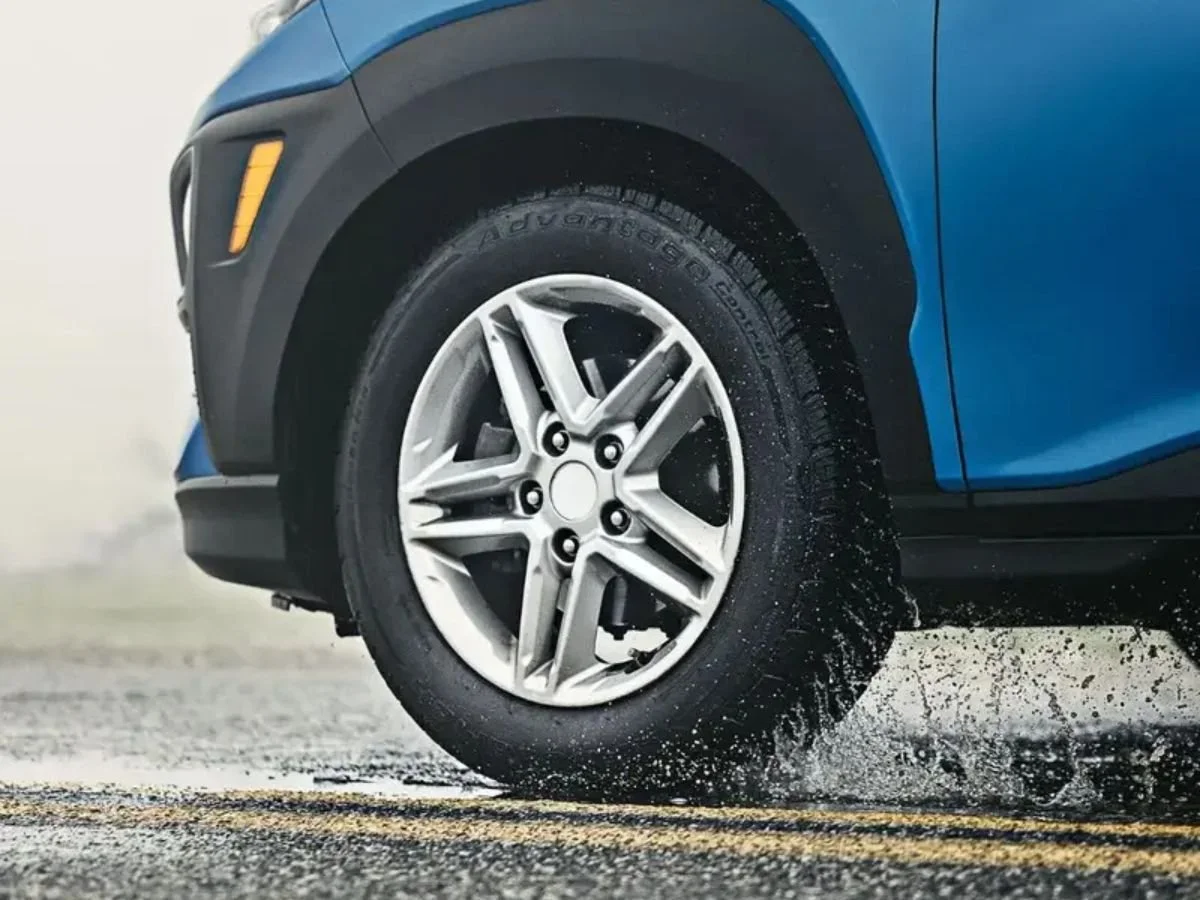 BFGoodrich Advantage Control tire on a blue vehicle driving through a puddle with a water splash.