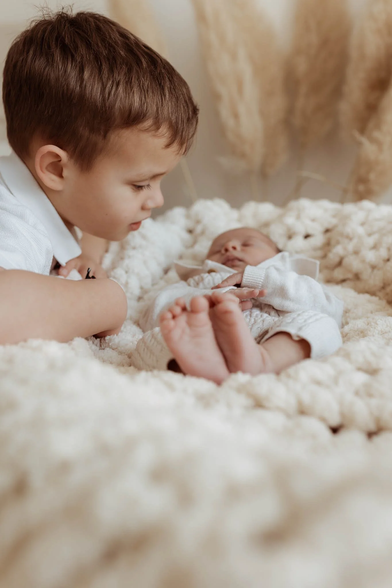 A young boy gently holding a newborn baby on a soft, cream-colored blanket.
