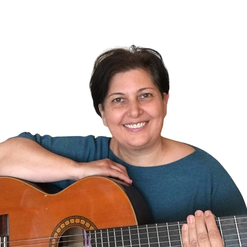 Woman with short dark hair playing an acoustic guitar, smiling, wearing a blue shirt, white background