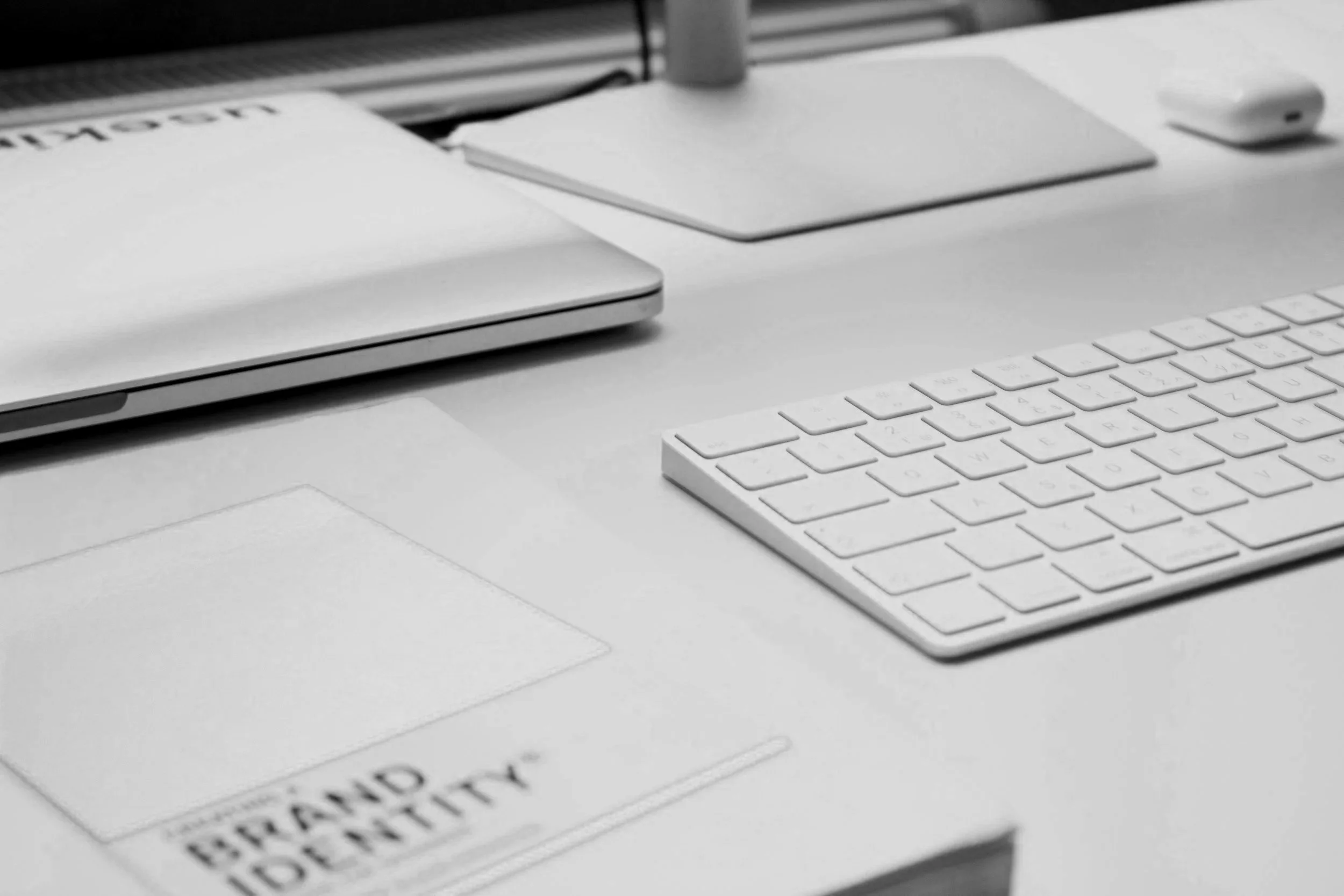 Close-up of an office desk with a white keyboard, a laptop, a wireless mouse, and a document with an orange cover.